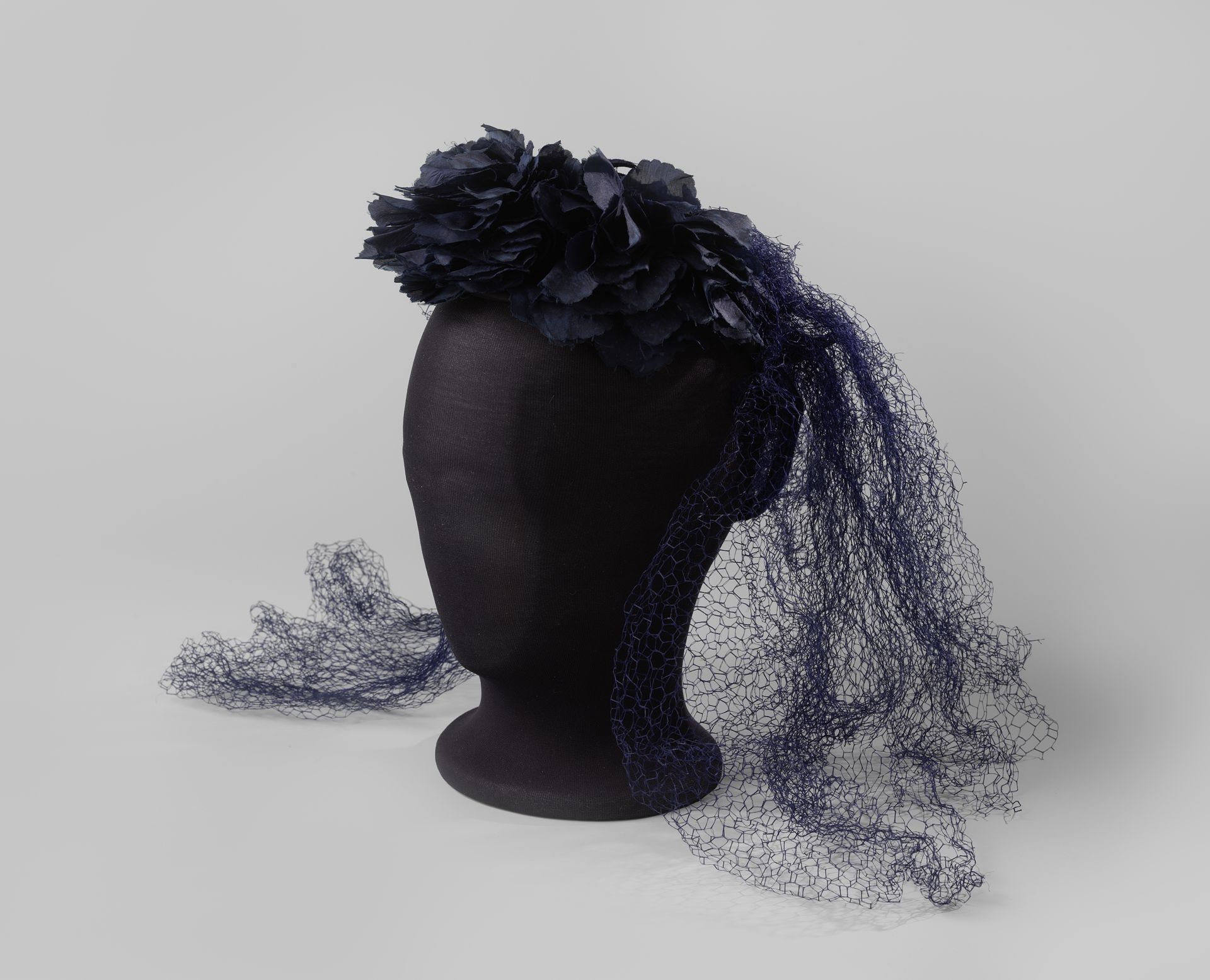 Bonnet-coiffure van marineblauwe bloemen van zijde en fluweel, verwerkt met blauwe voile, op een ijzerdraadframe in hoefijzervorm by H. van Dooren & Cie