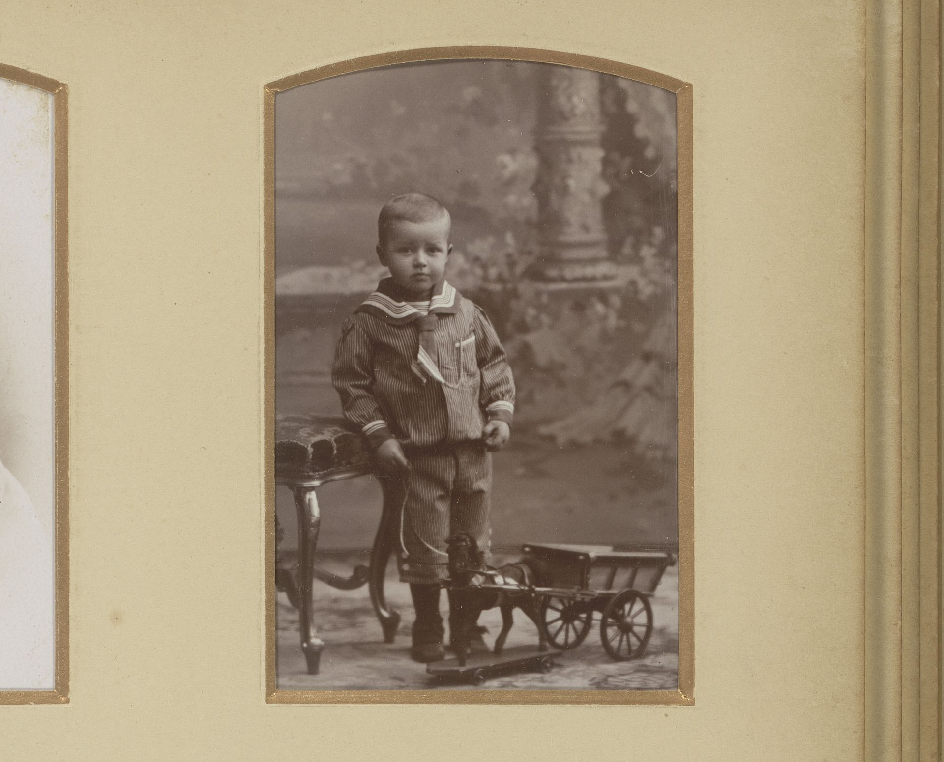 Portret van een staande jongen in matrozenpak met speelgoed paard en wagen by Machiel Hendricus Laddé