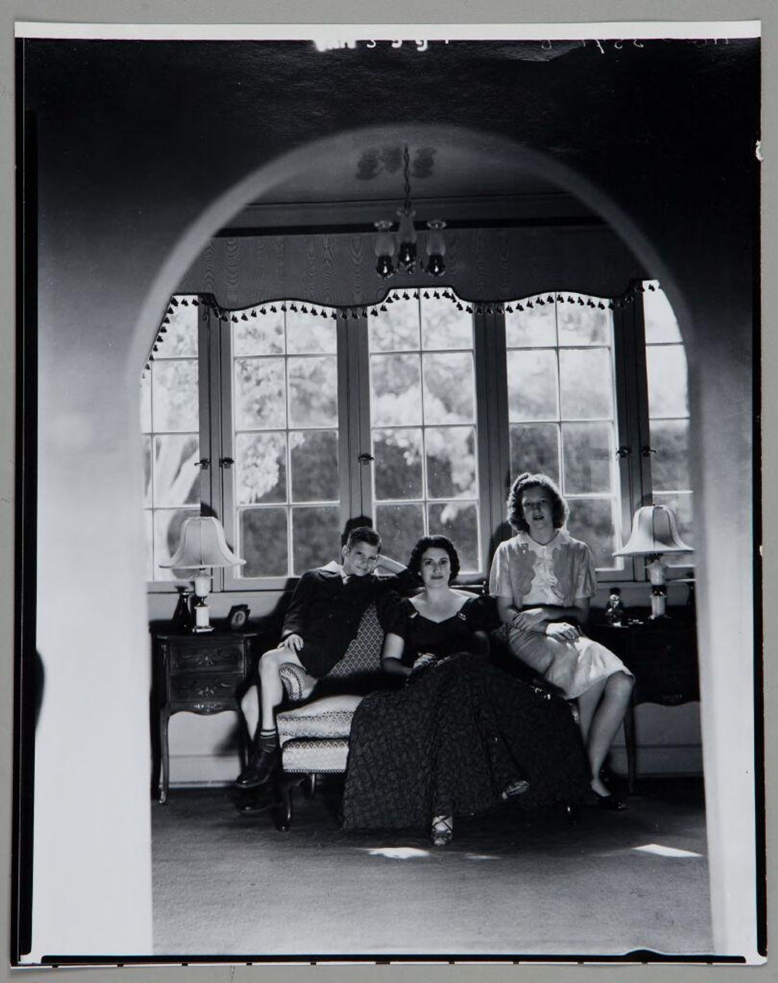 Untitled (woman seated on loveseat between two older children, seen through archway) by Paul Gittings