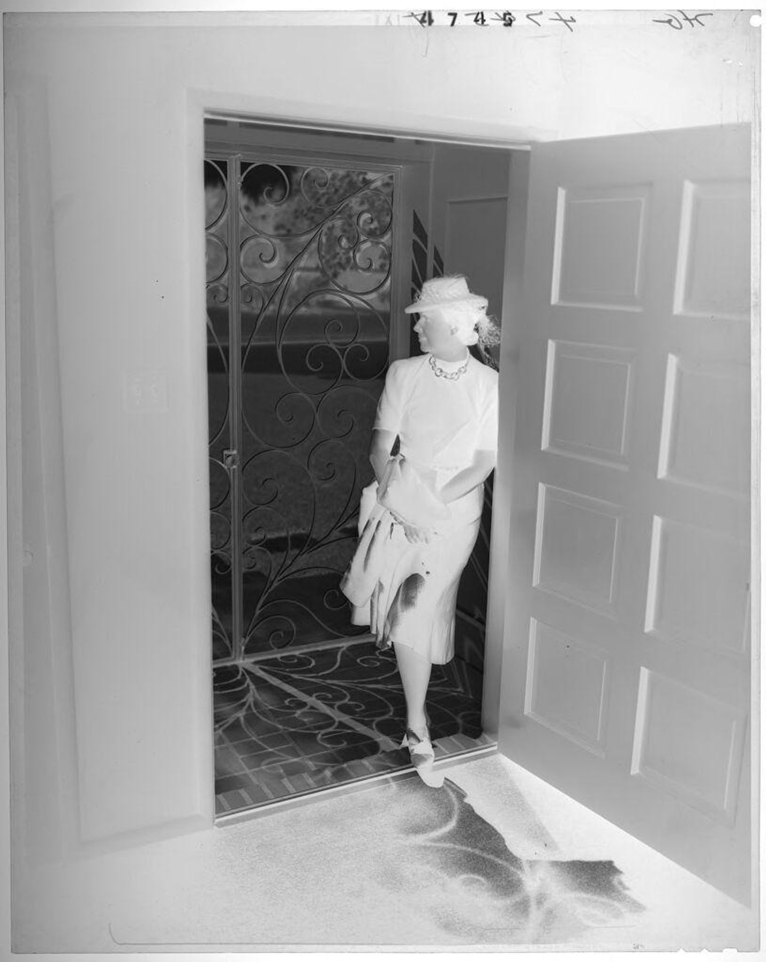 Untitled (woman in hat standing in vestibule between doors, looking away) by Paul Gittings