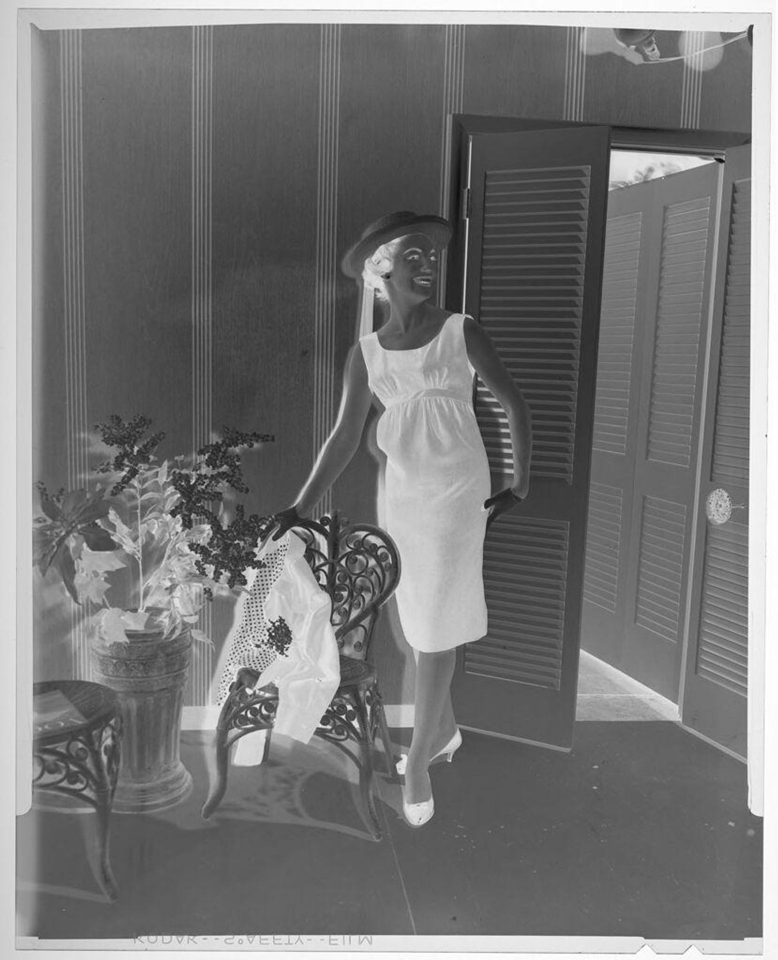 Untitled (fashion portrait of woman in summer dress and hat standing in stylized pose next to chair) by Martin Schweig