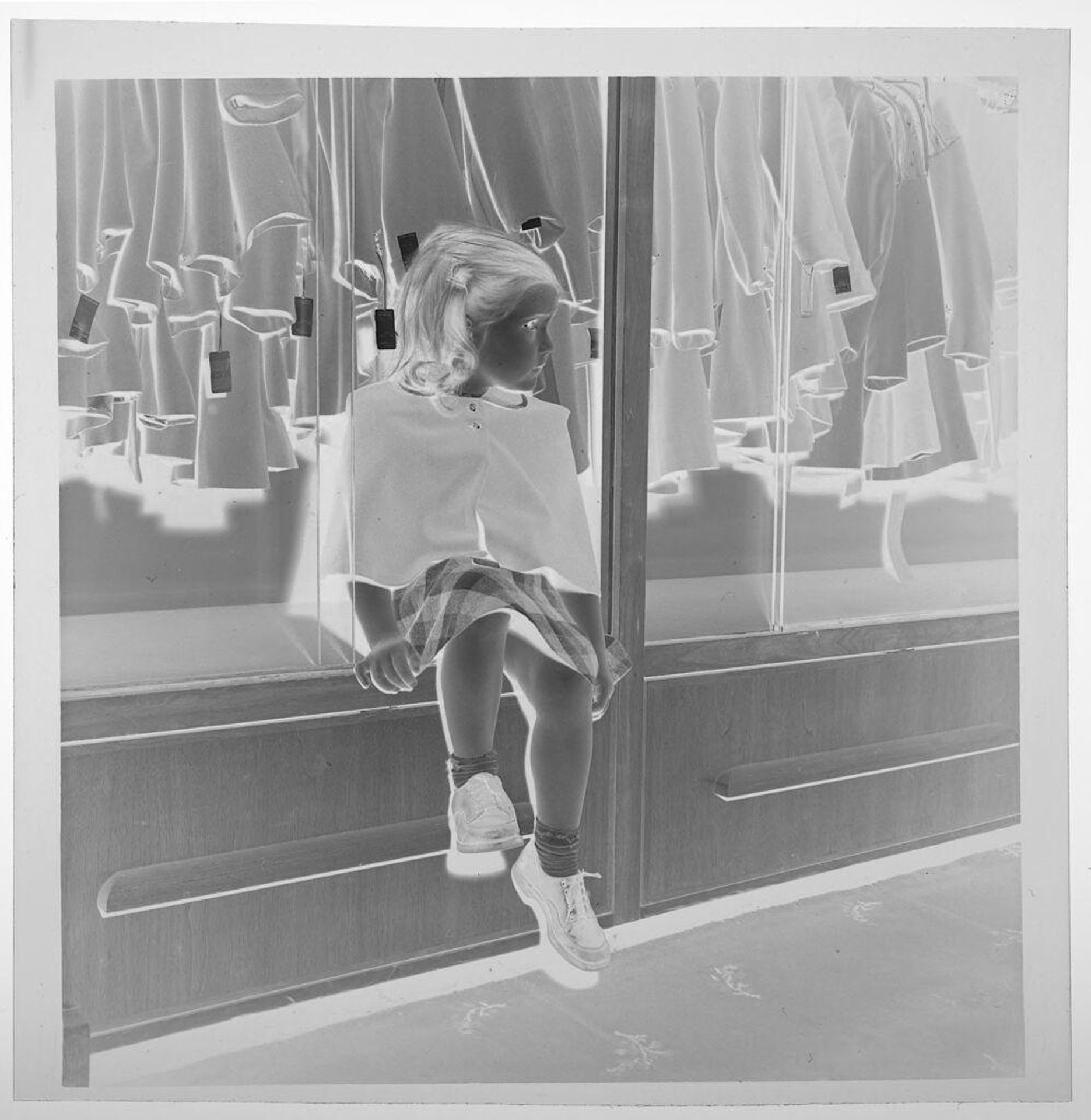 Untitled (young girl seated on ledge of shop clothes display) by Jack Gould