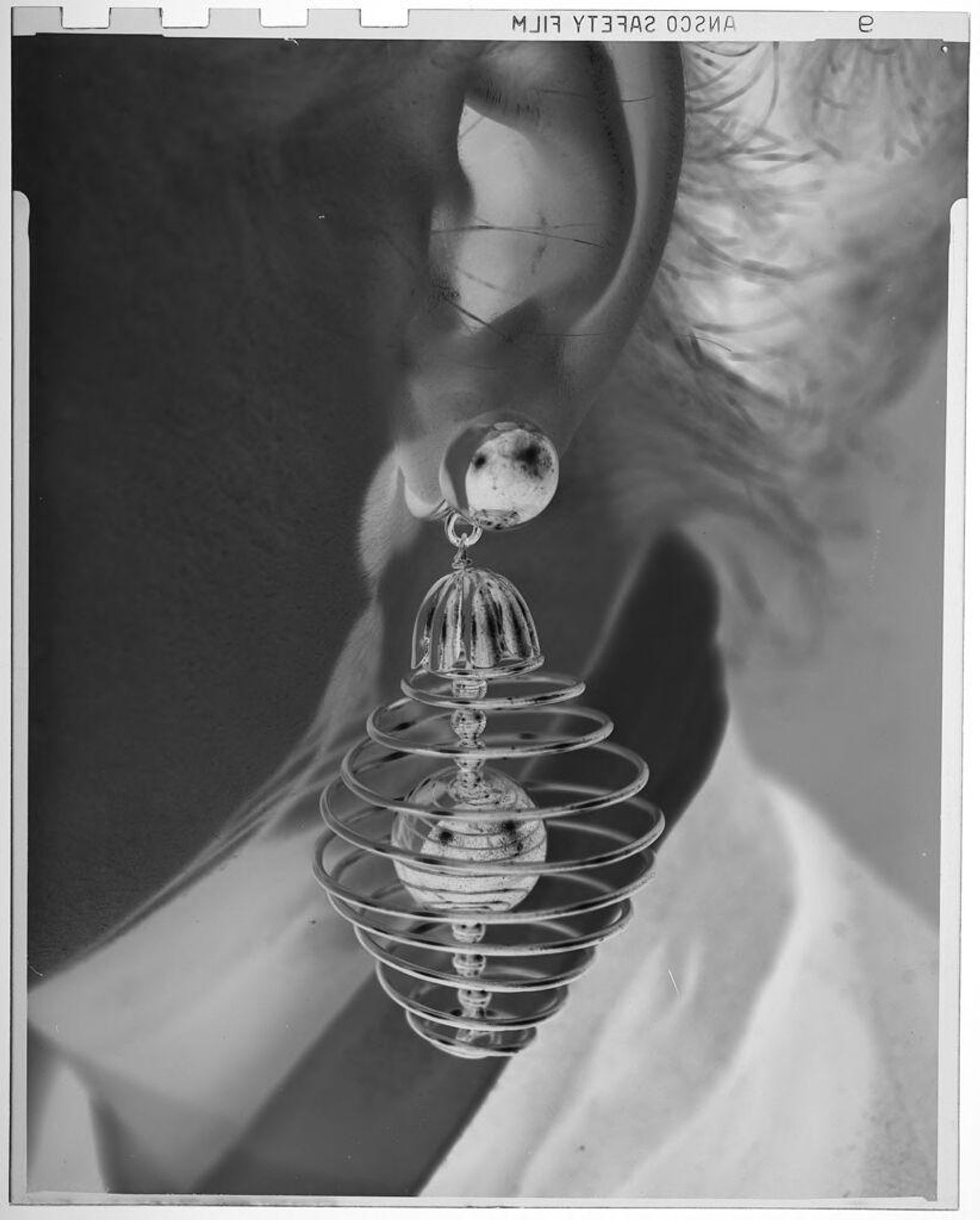 Untitled (close-up view of woman's earring, spiral silver with sphere in center) by Jack Gould