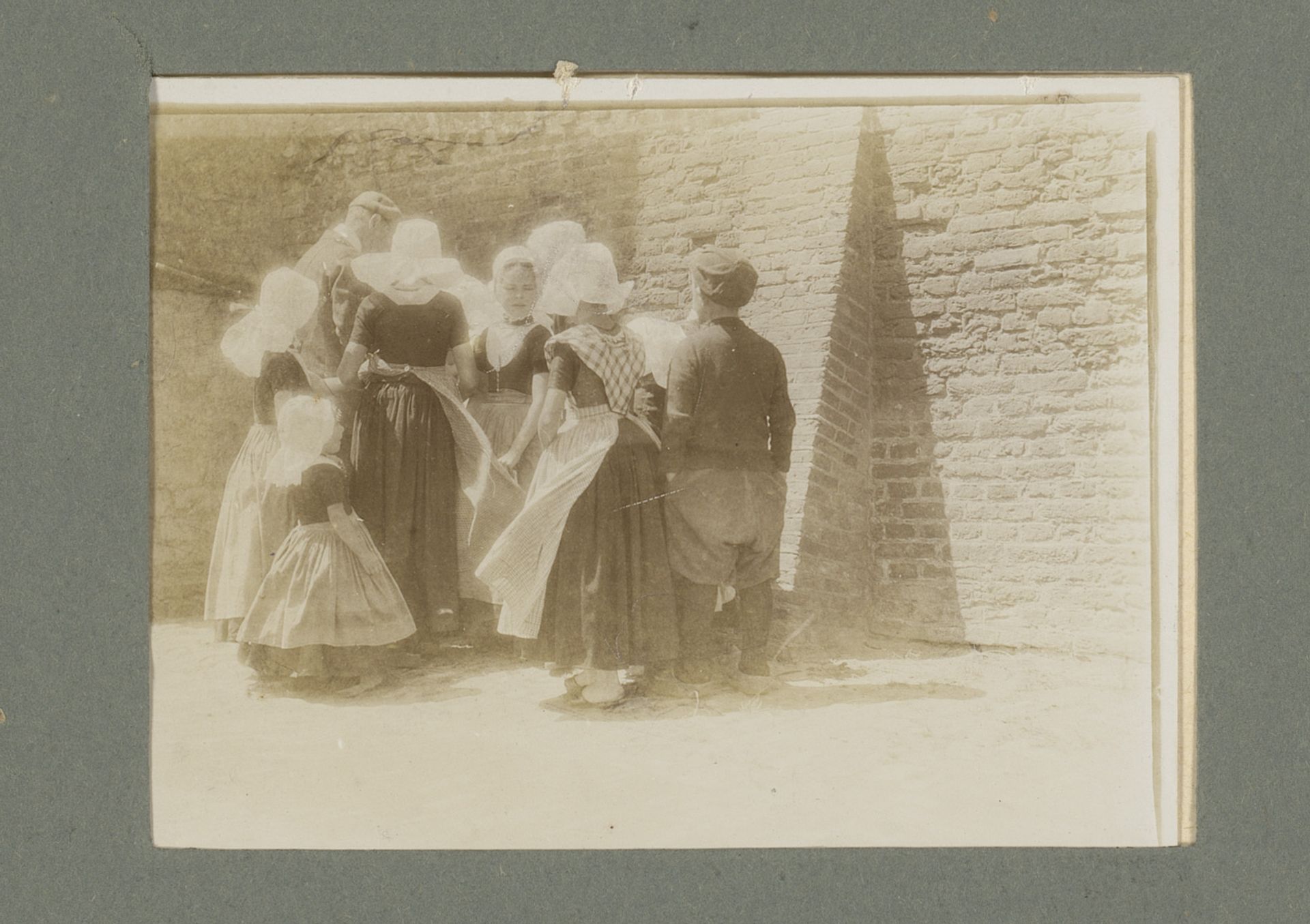 Groep mensen in klederdracht, staande voor een muur van een gebouw by G. Hidderley