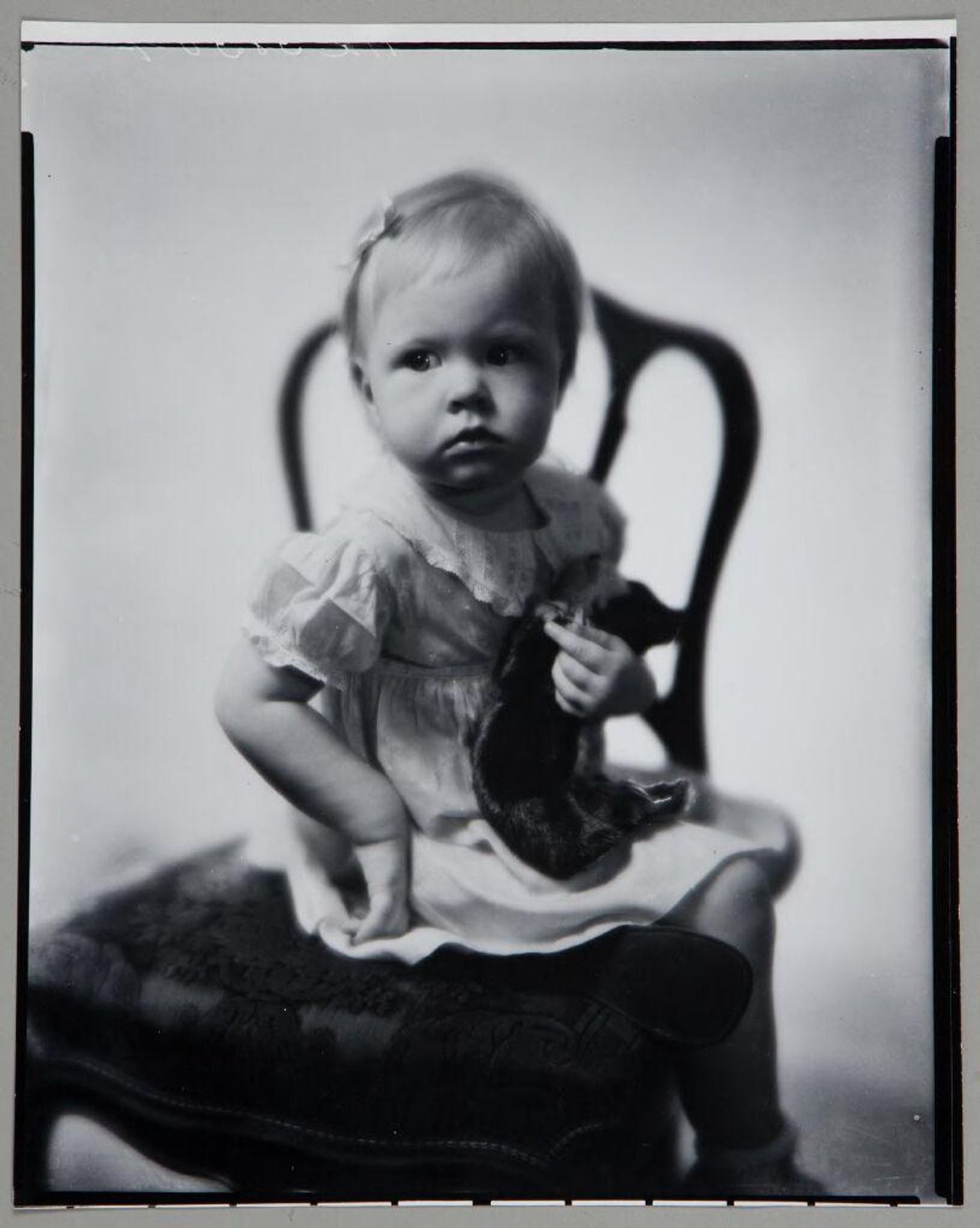 Untitled (small child seated on chair, holding stuffed animal) by Paul Gittings