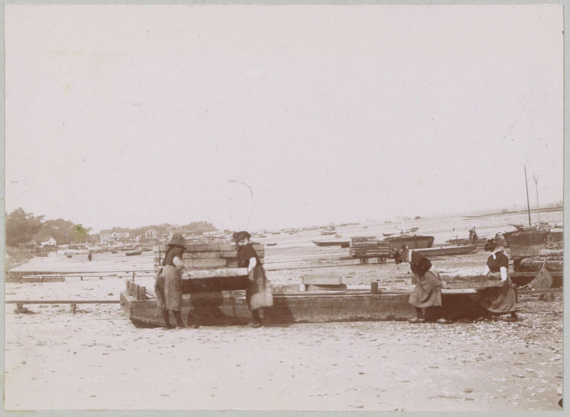 Vissersvrouwen sjouwen (vermoedelijk) bakken met vangst op het strand bij Arcachon by Delizy
