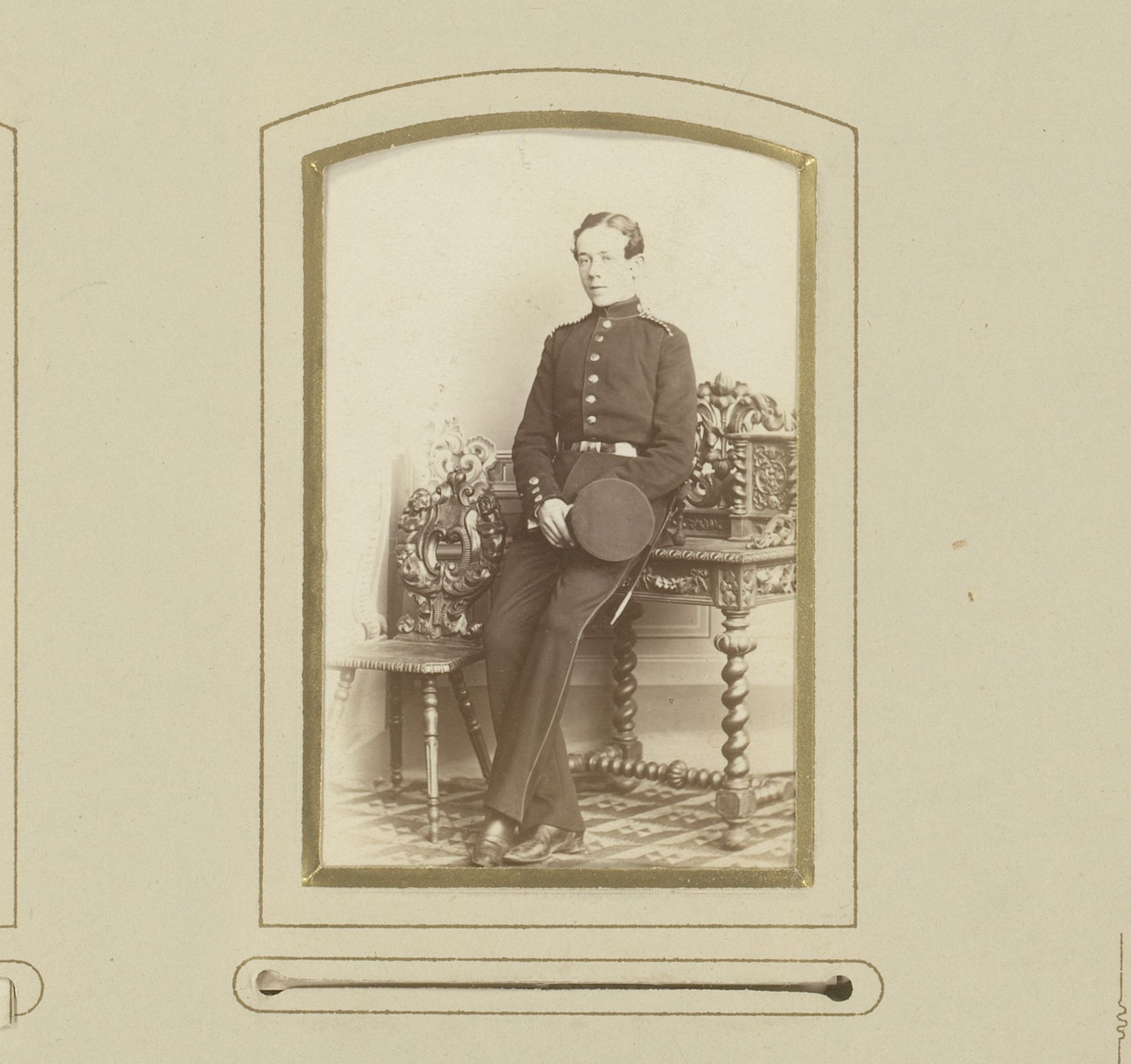 Portret van een jonge man in uniform met pet in de hand, leunend op een schrijftafel by Leopold Wallnau