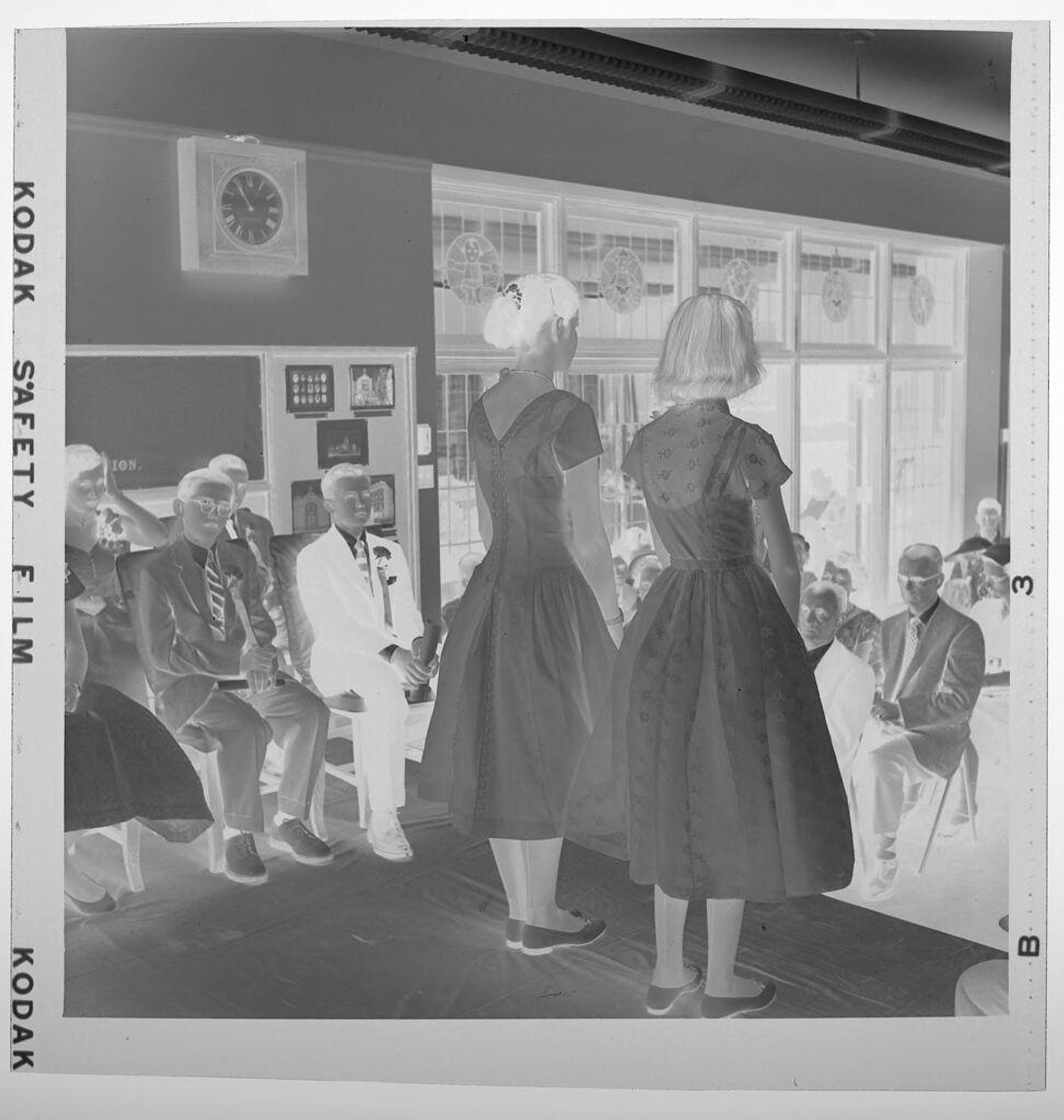 Untitled (graduation; girls in dresses standing on stage, boys seated) by Jack Gould
