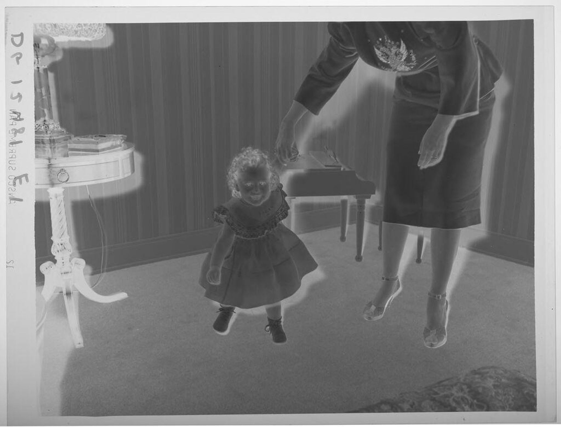 Untitled (little girl in dress holding mother's hand in living room as she leans forward) by Paul Gittings