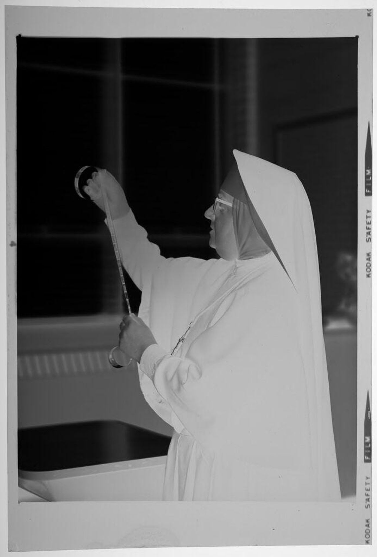 Untitled (nun looking at 35mm negatives inside school room) by Martin Schweig