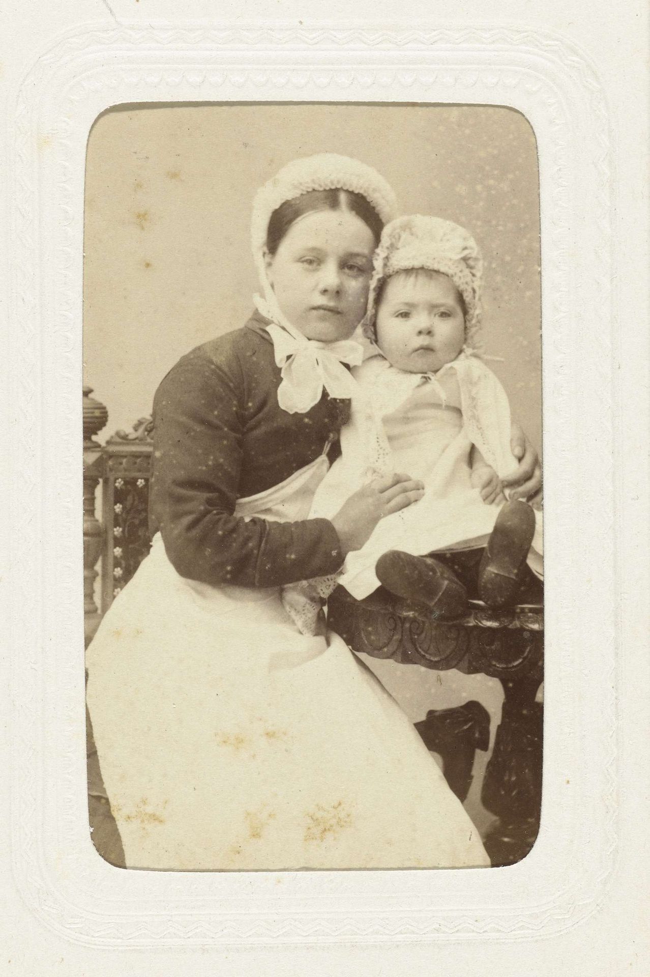 Studioportret van een vrouw met babay, beiden met een wit kapje op het hoofd by J.H. v.d. Heijden