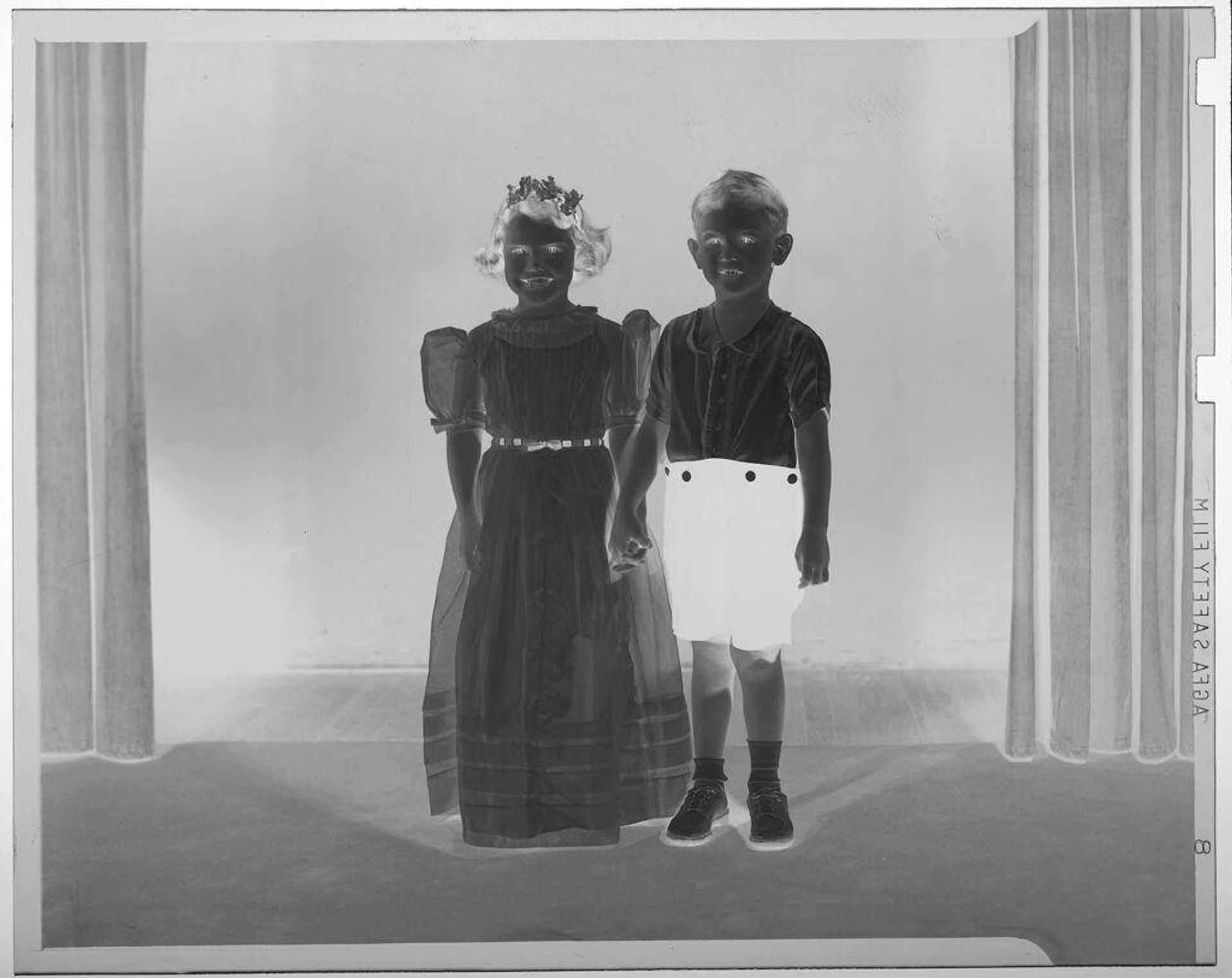 Untitled (boy and girl in costumes posed holding hands between two curtains) by Martin Schweig