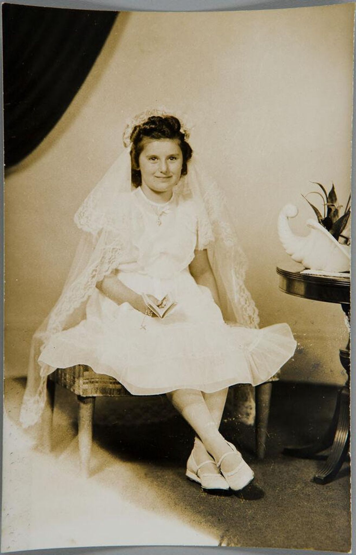 Untitled (girl seated in white, wearing veil, holding bible and rosary) by John Deusing