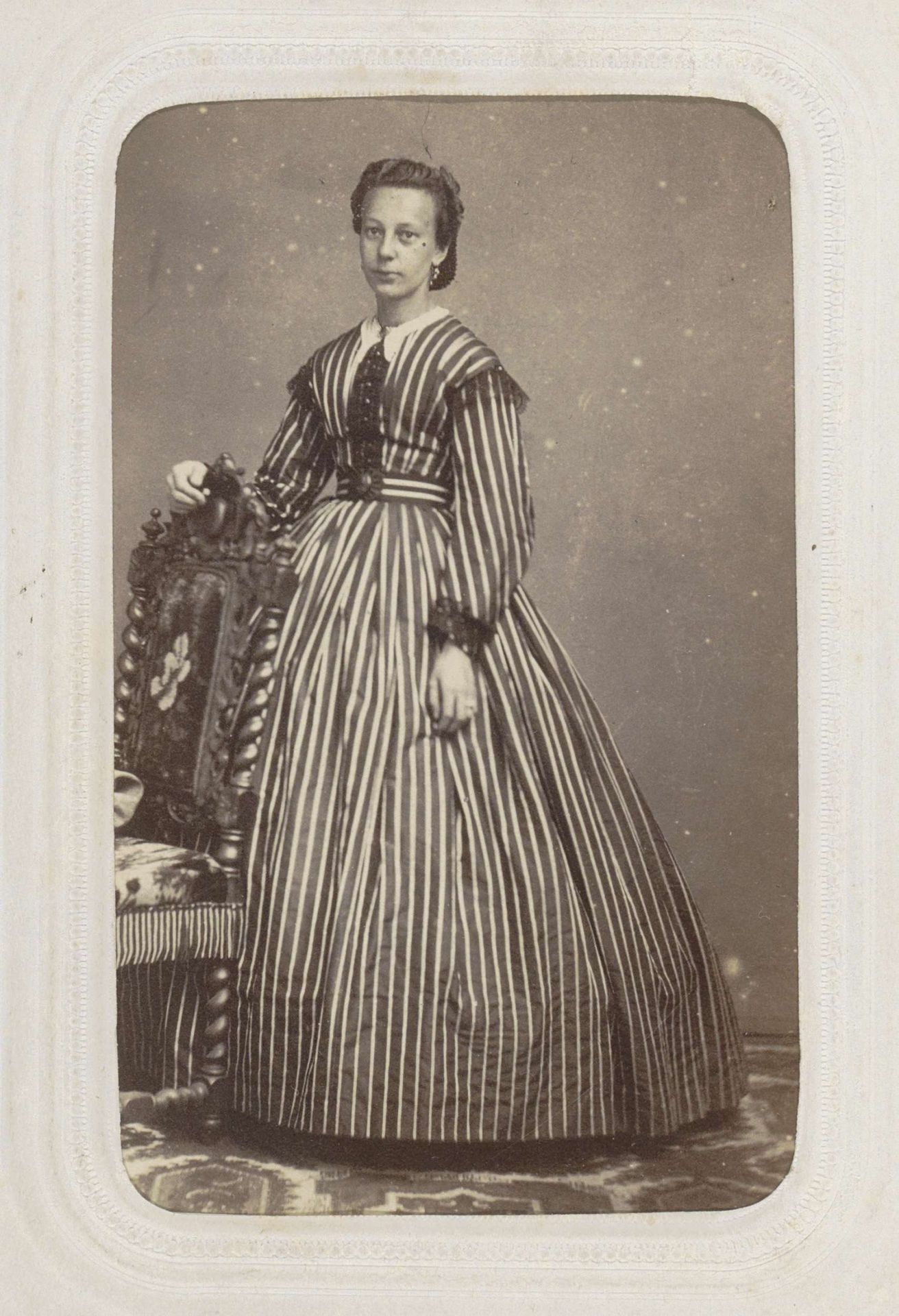 Portret van een vrouw in een gestreepte lange jurk, staand bij een stoel by Leonard Stollenwerk