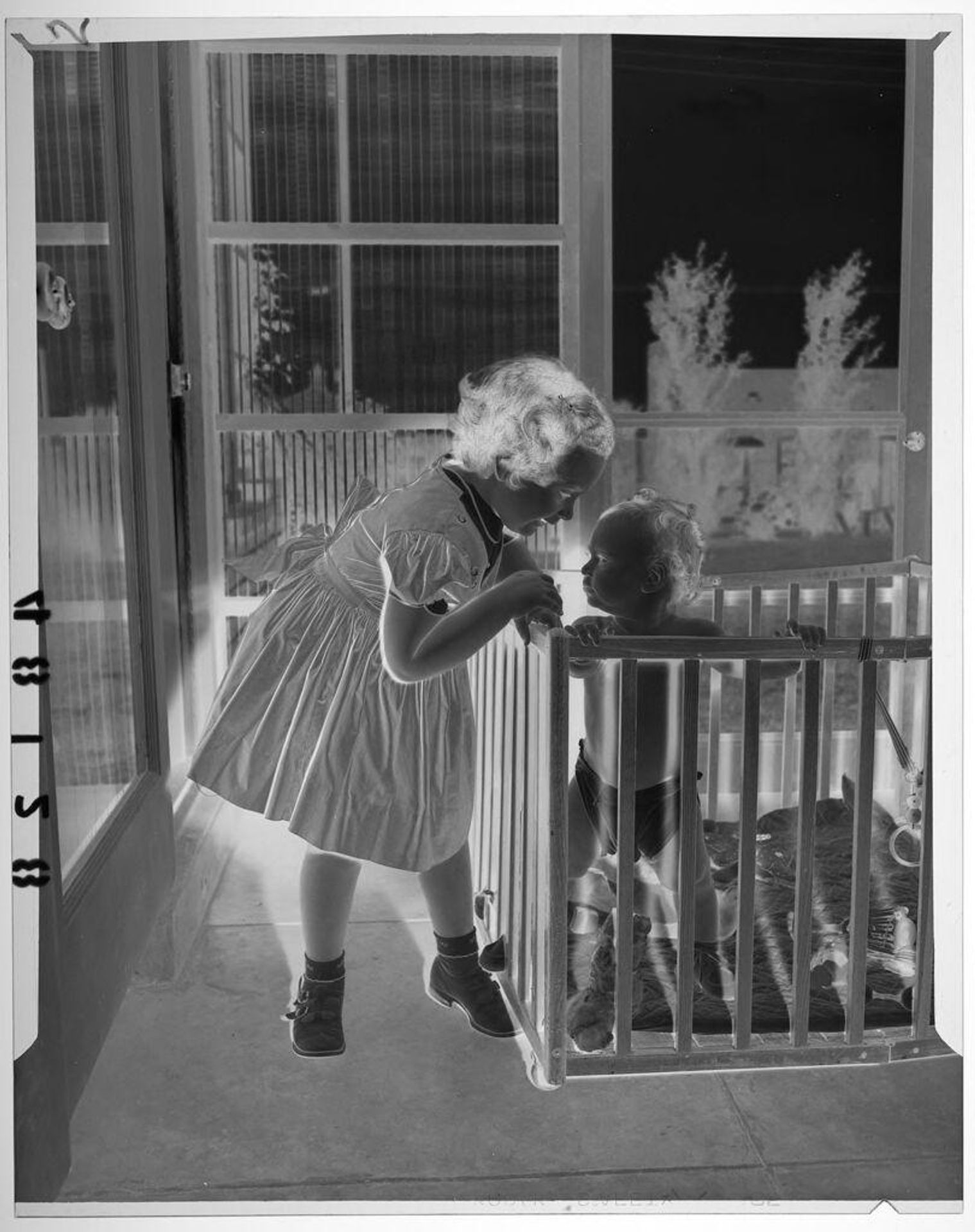 Untitled (young girl posed looking at baby boy in playpen) by Martin Schweig