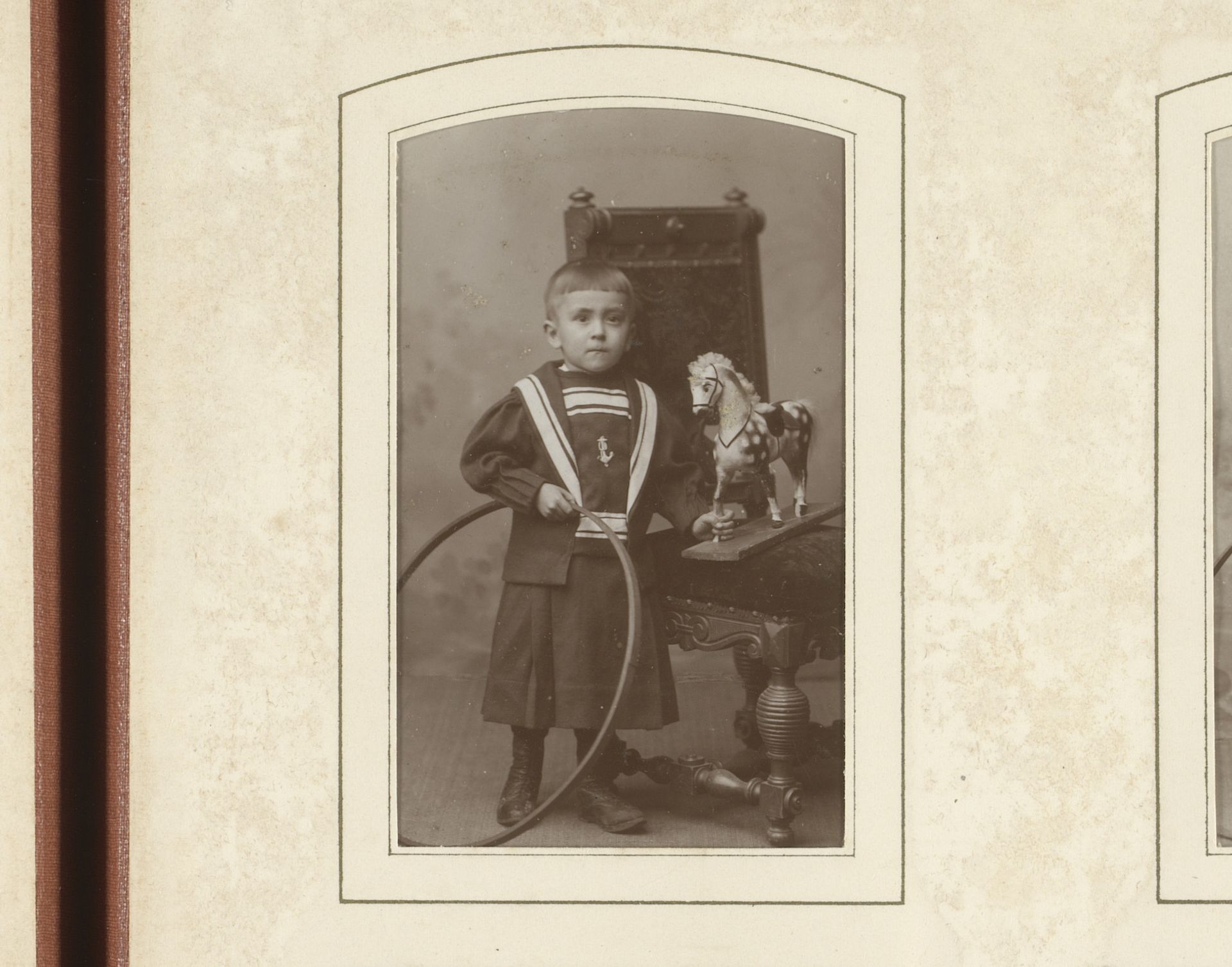 Portret van een jongen met hoepel in de hand, staand bij een stoel met speelgoed paard by W.G. Kuijer & Zonen