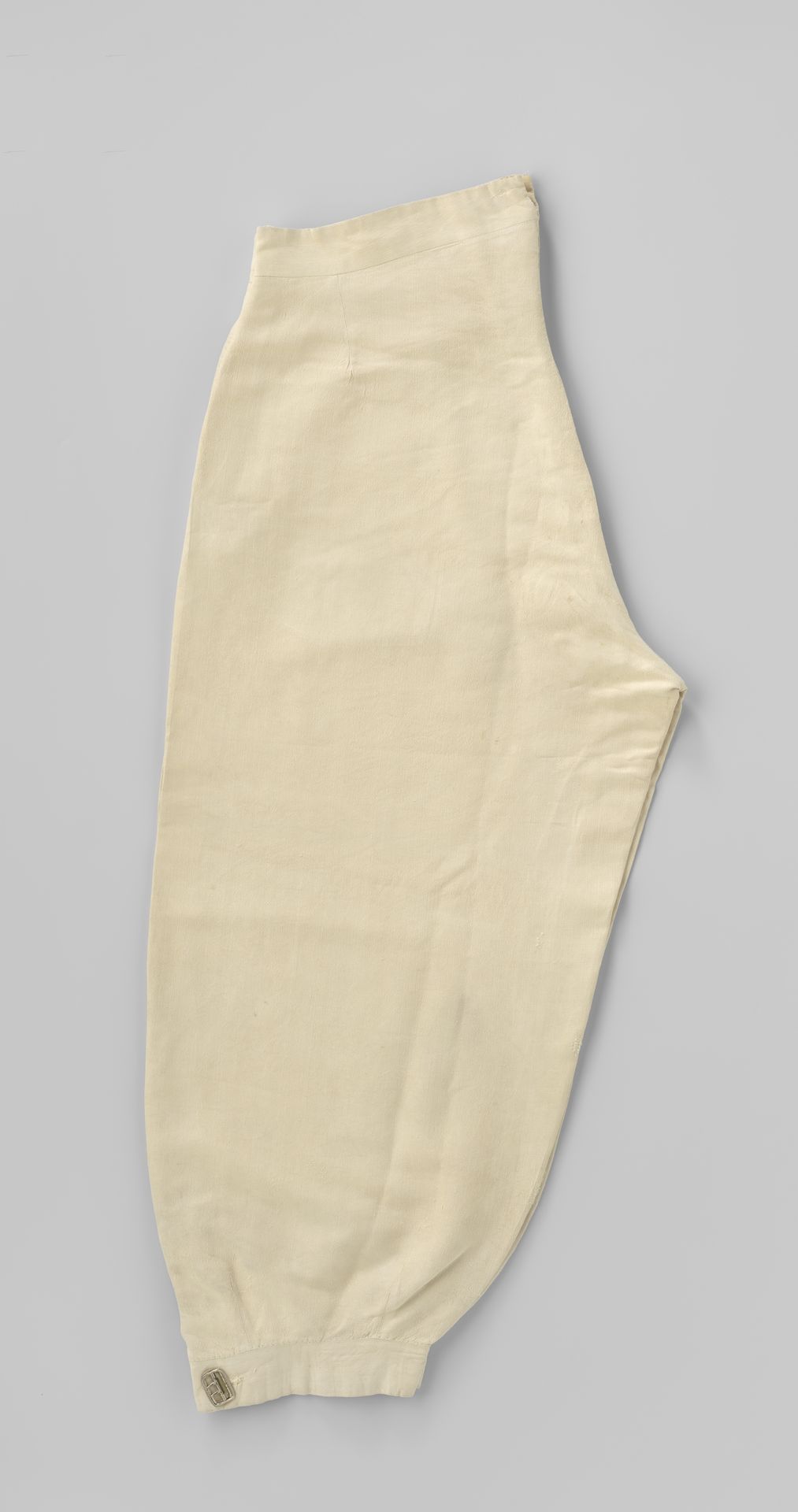 Broek in plus-fourmodel van beige katoen, met steekzakken in de zijnaden, gulp met benen knopen, onderaan een gespsluiting en aan de binnenkant van de taille acht knopen by Kerslane & Dixon
