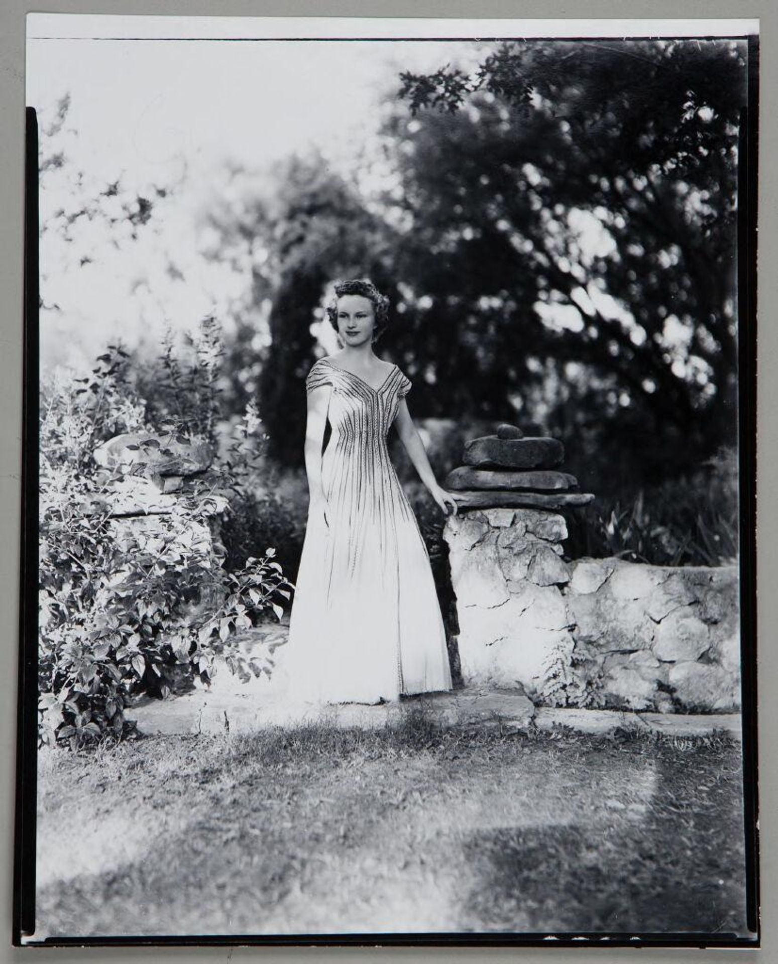 Untitled (young woman in off-shoulder dress standing outdoors by rock wall) by Paul Gittings