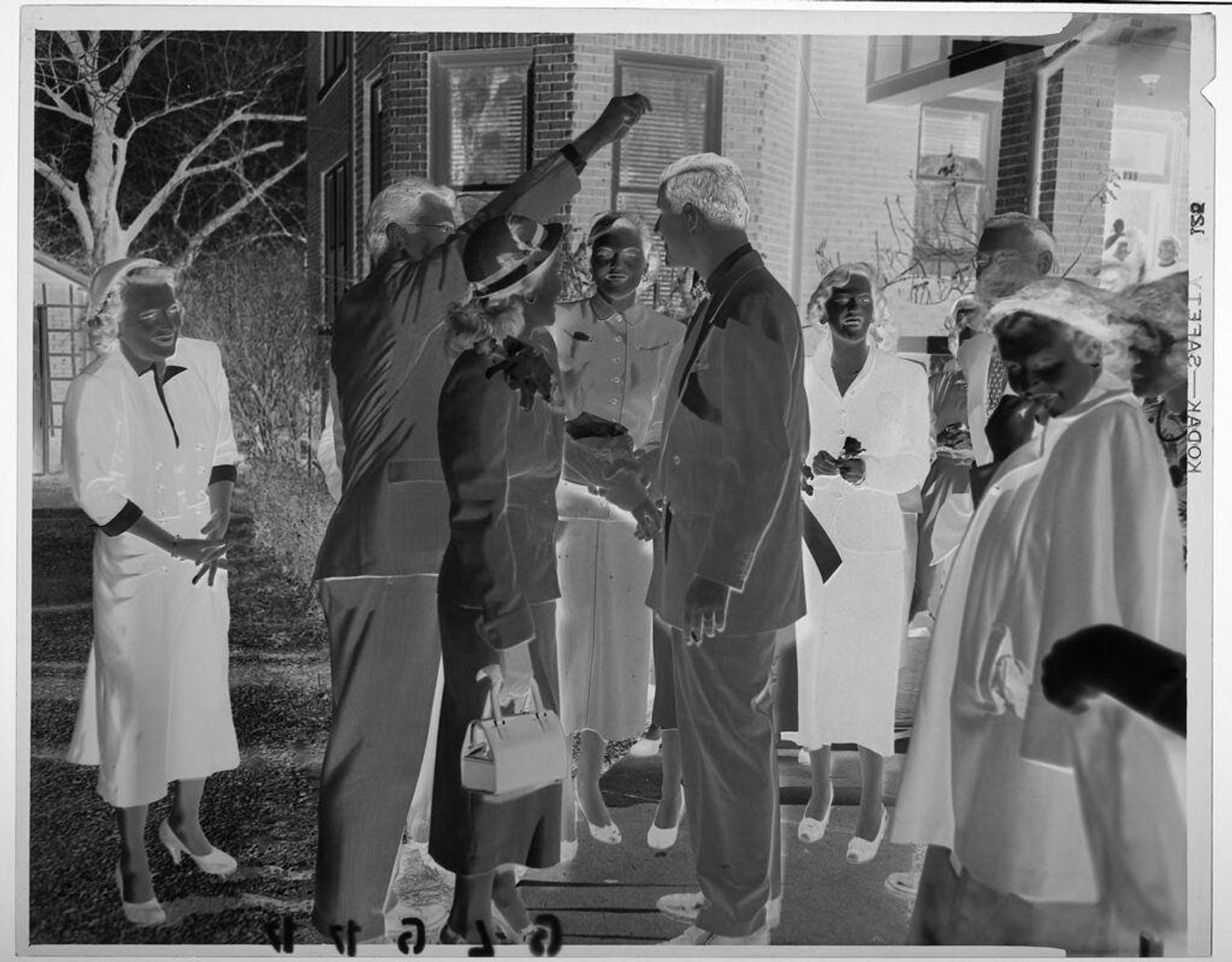 Untitled (group standing around outside of home laughing with one man raising arm above another) by Martin Schweig