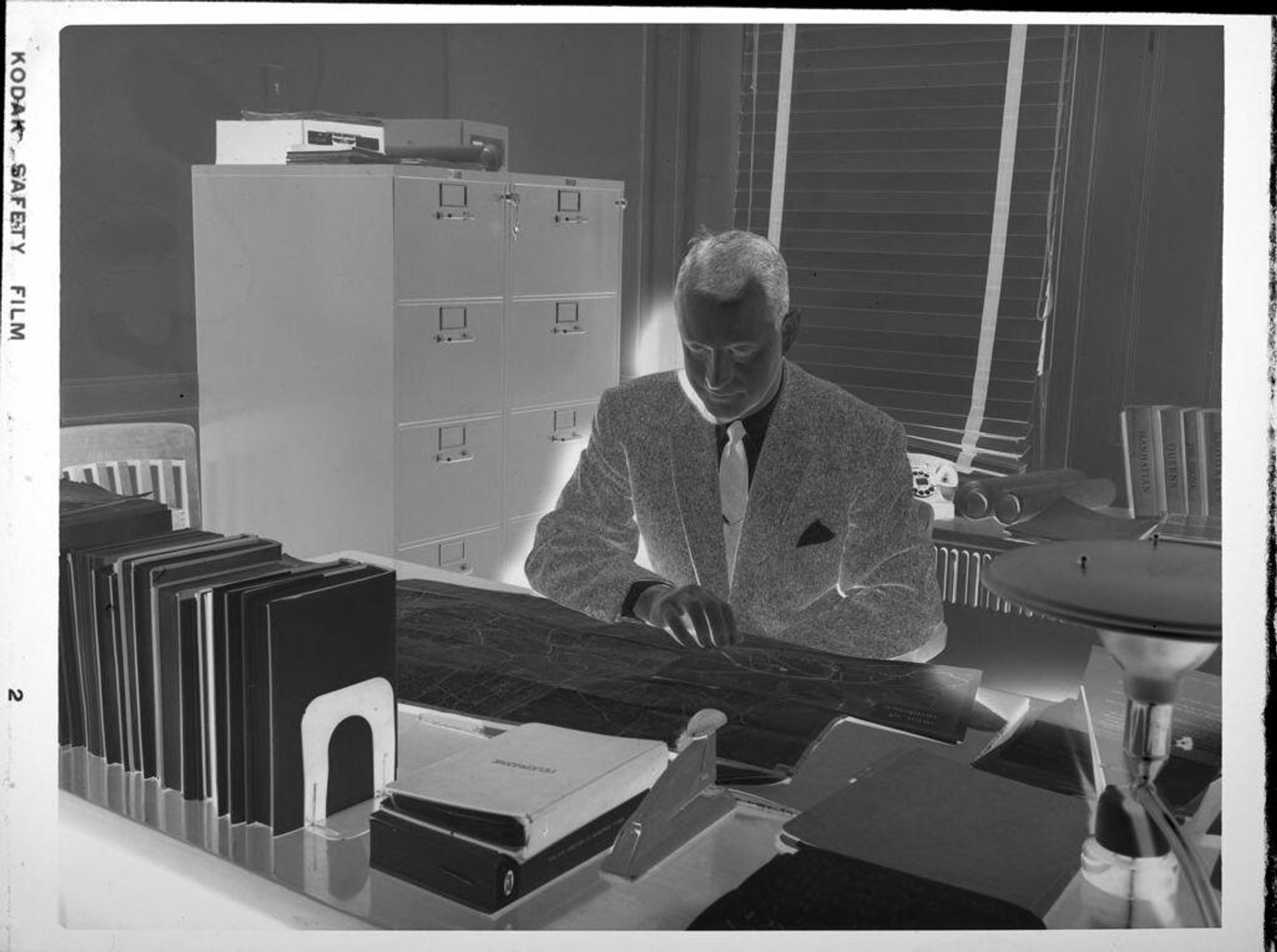 Untitled (man at desk, looking at map) by Peter James Studio