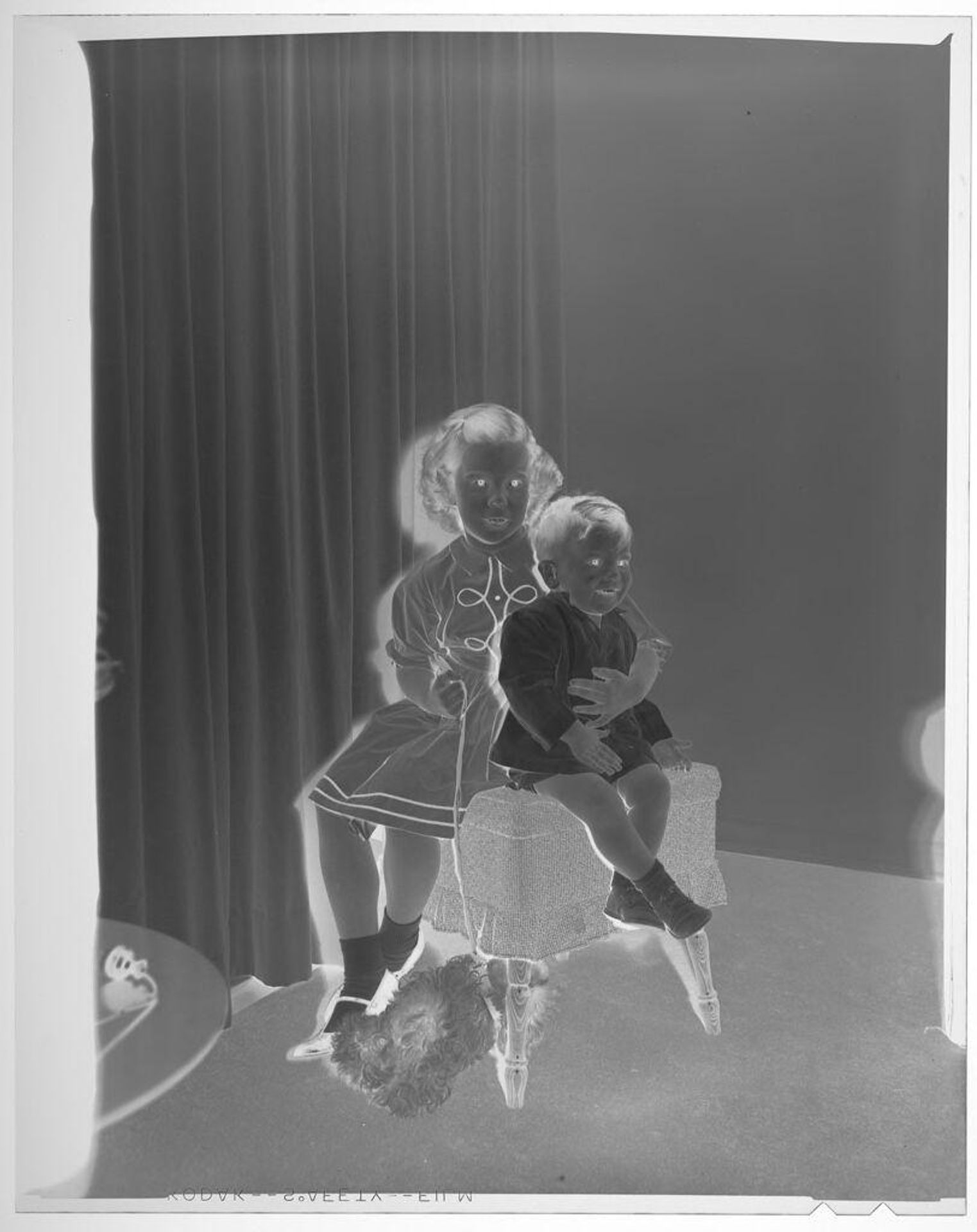 Untitled (young girl and young boy posed sitting on ottoman with dog beneath it) by Martin Schweig