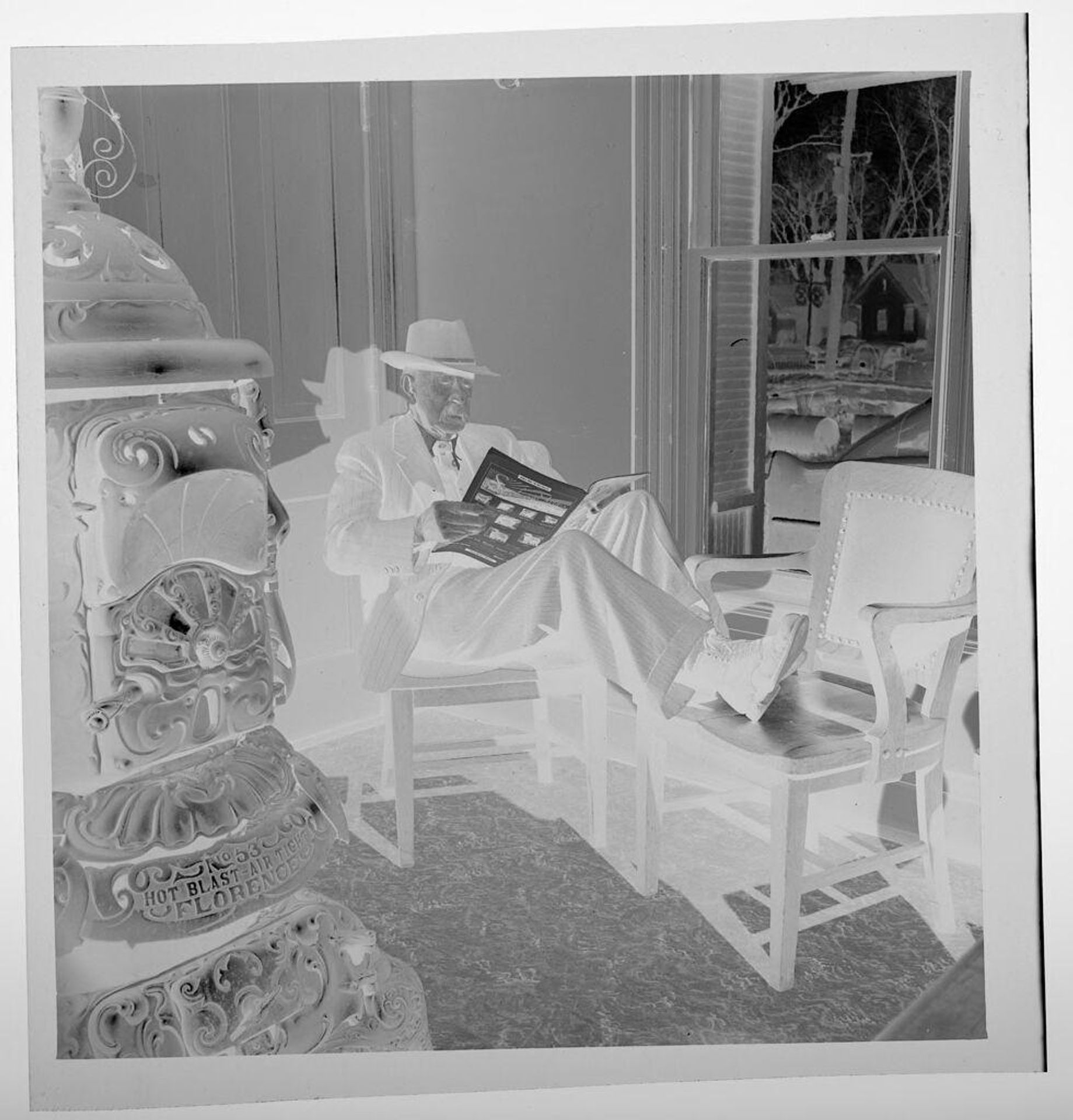 Untitled (man reading in chair, next to wood stove) by Jack Gould