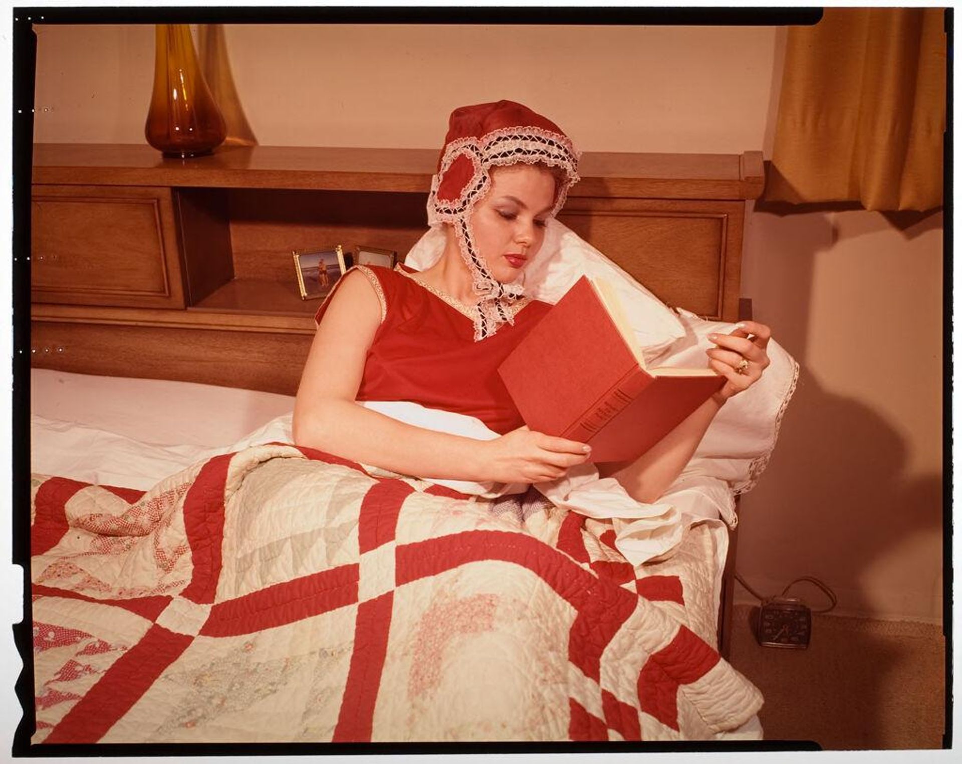 Untitled (woman in bed reading and wearing red nightcap) by Jack Gould