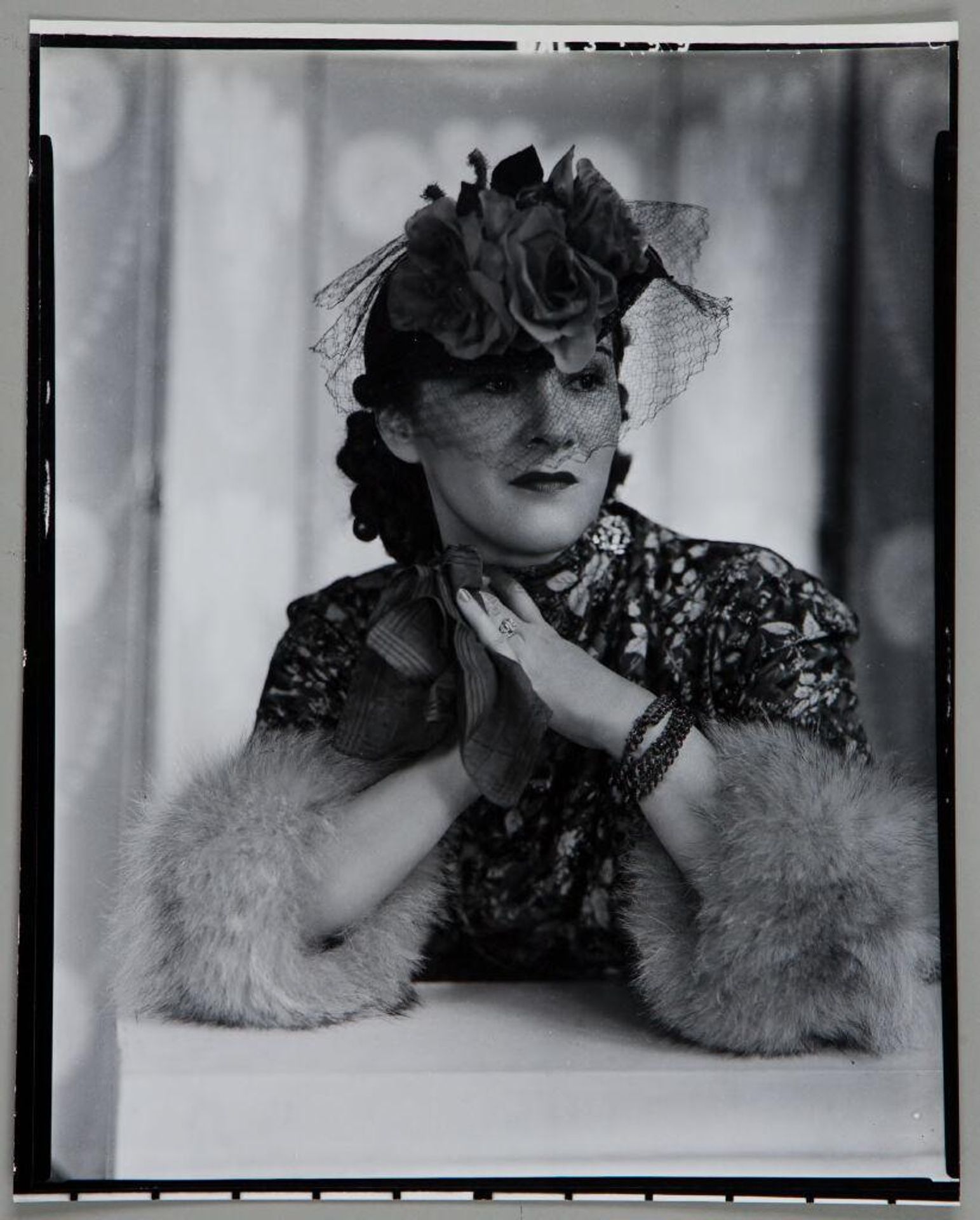 Untitled (portrait of woman in floral dress, laced hat, and fur trimmed cuffs leaning on elbows and holding hanky) by Paul Gittings