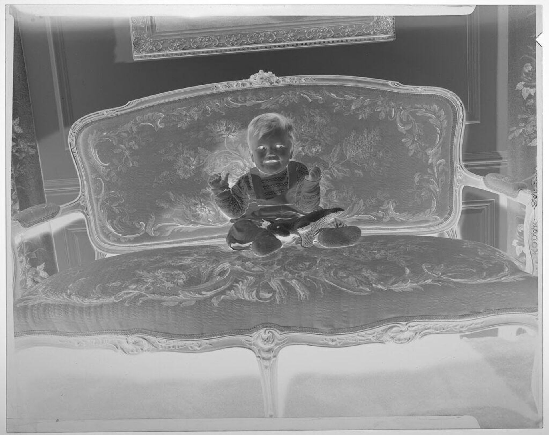 Untitled (baby posed sitting on ornate couch with toy horse in lap) by Martin Schweig