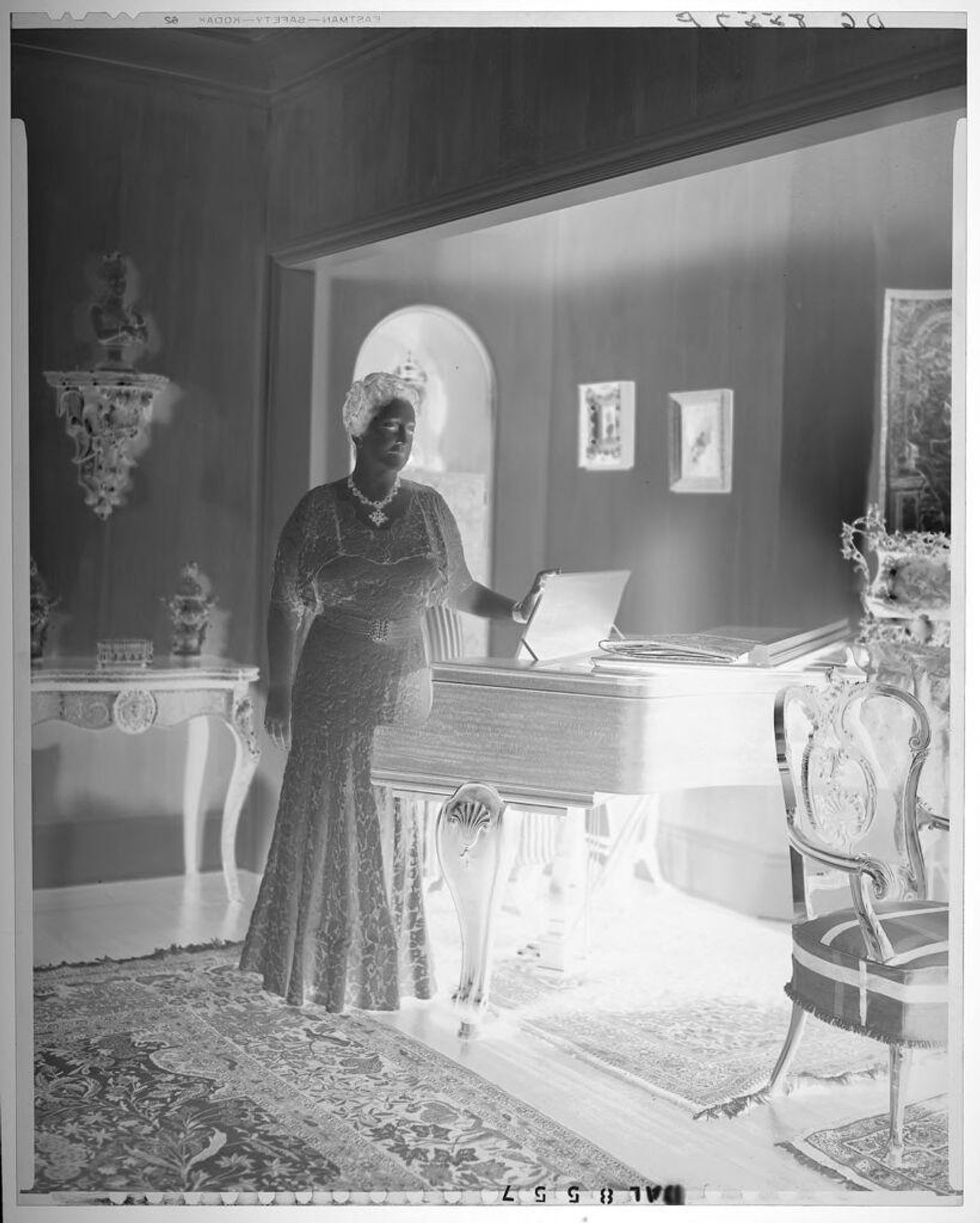 Untitled (woman in evening dress standing by baby grand piano) by Paul Gittings