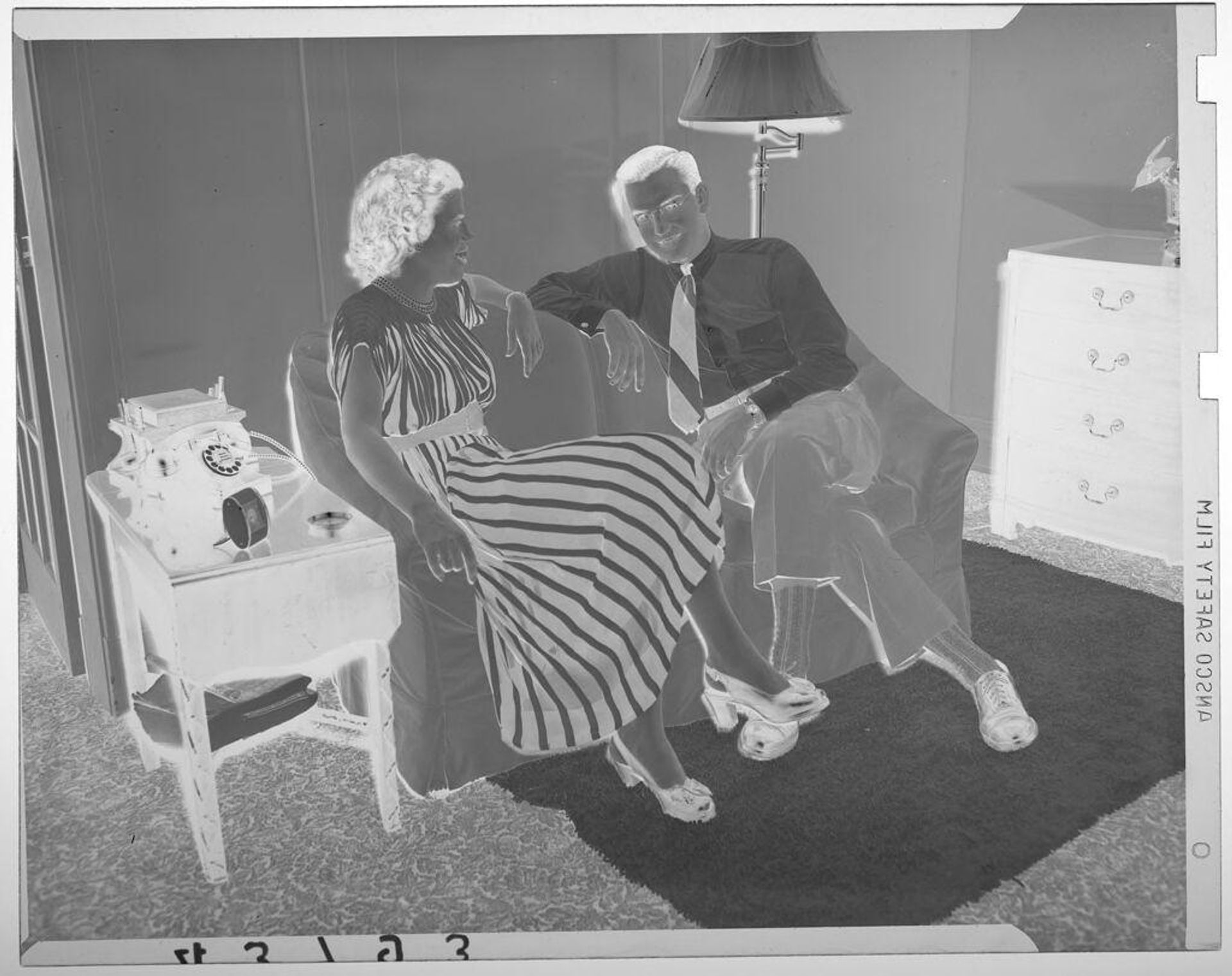 Untitled (woman in striped dress posed with man in glasses on small couch in living room) by Martin Schweig