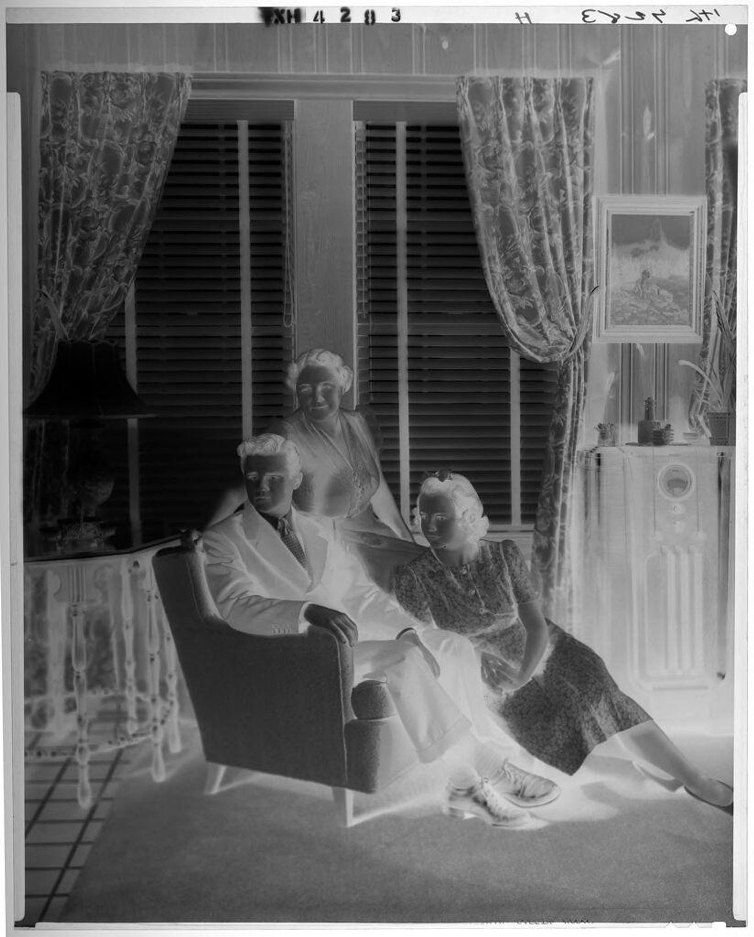 Untitled (mother with son and daughter seated on and around armchair in front of living room windows) by Paul Gittings