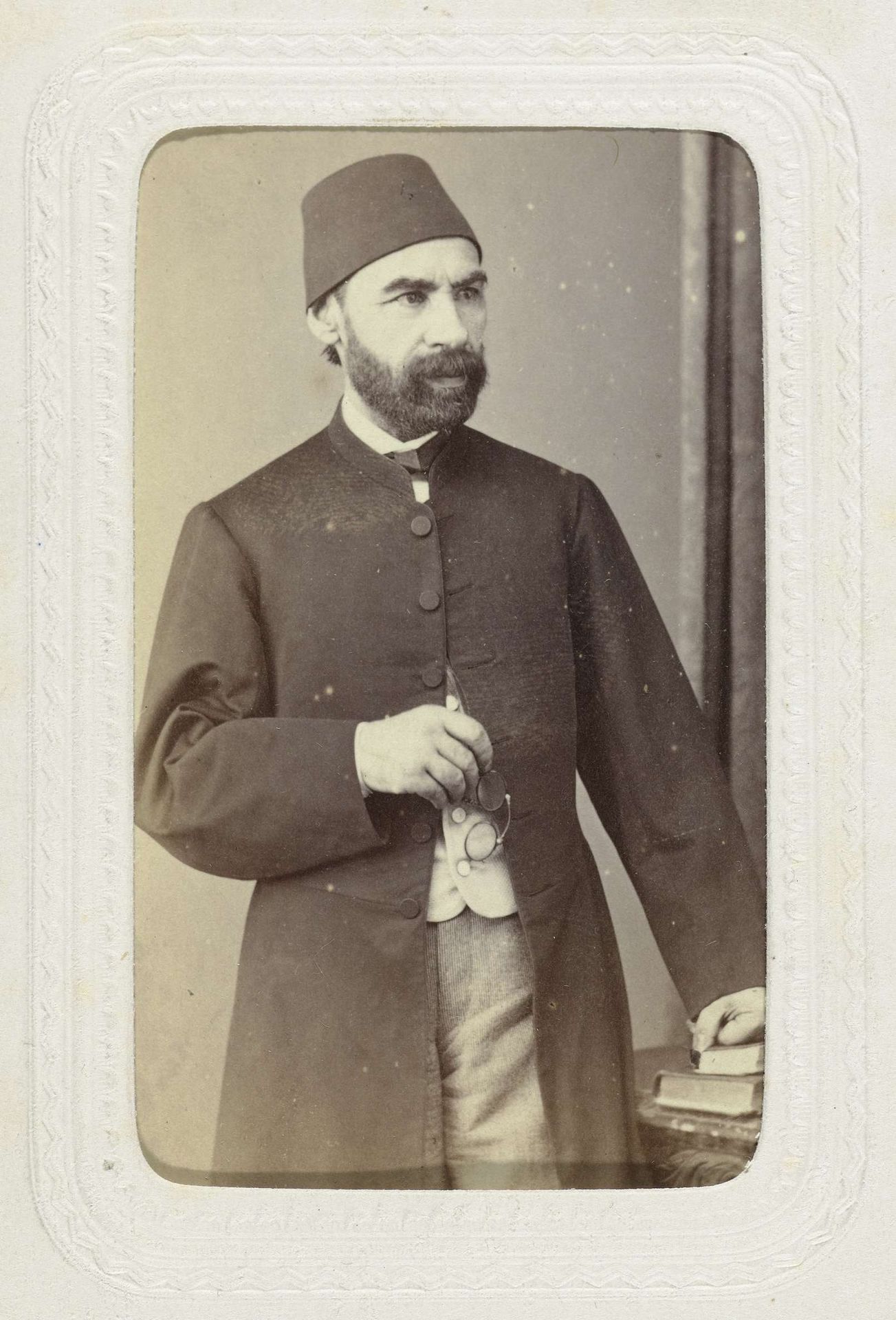 Studioportret van een man in lange jas met op zijn hoofd een fez by Abdullah Frères