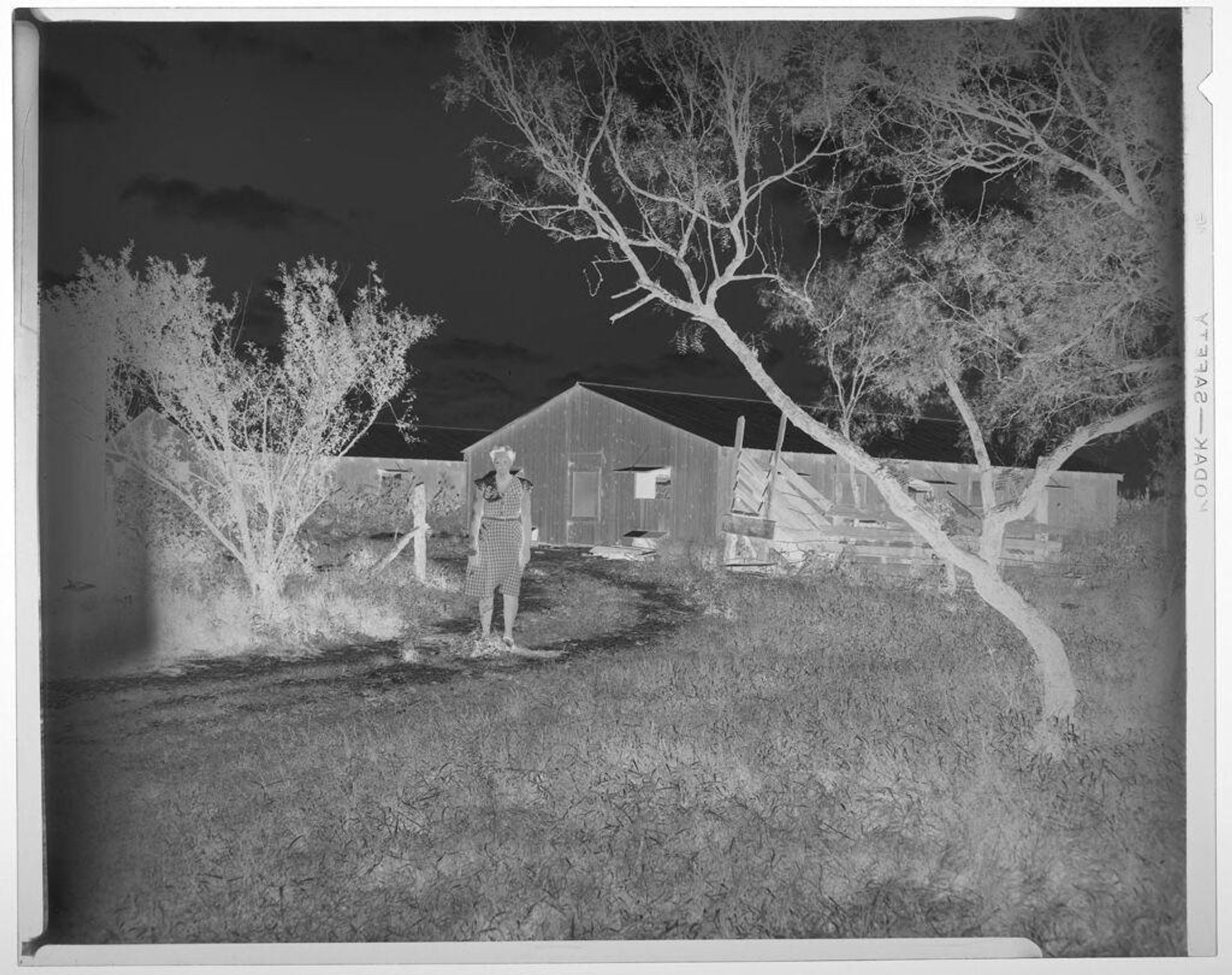 Untitled (woman standing on path outside buildings, Armo Mills Broiler operations) by Harry Annas