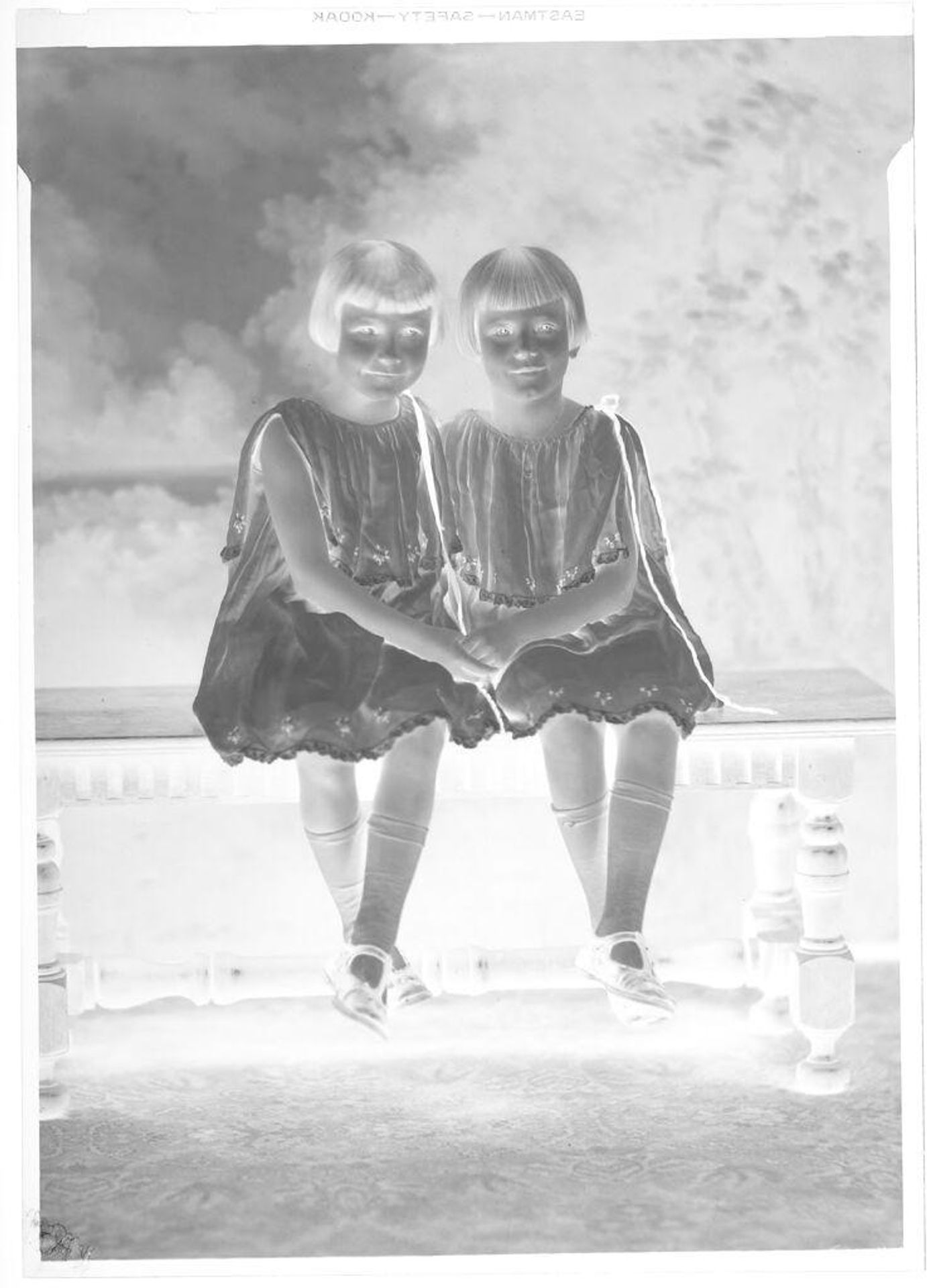 Untitled (twin girls seated on bench holding hands in matching dresses) by Hamblin Studio