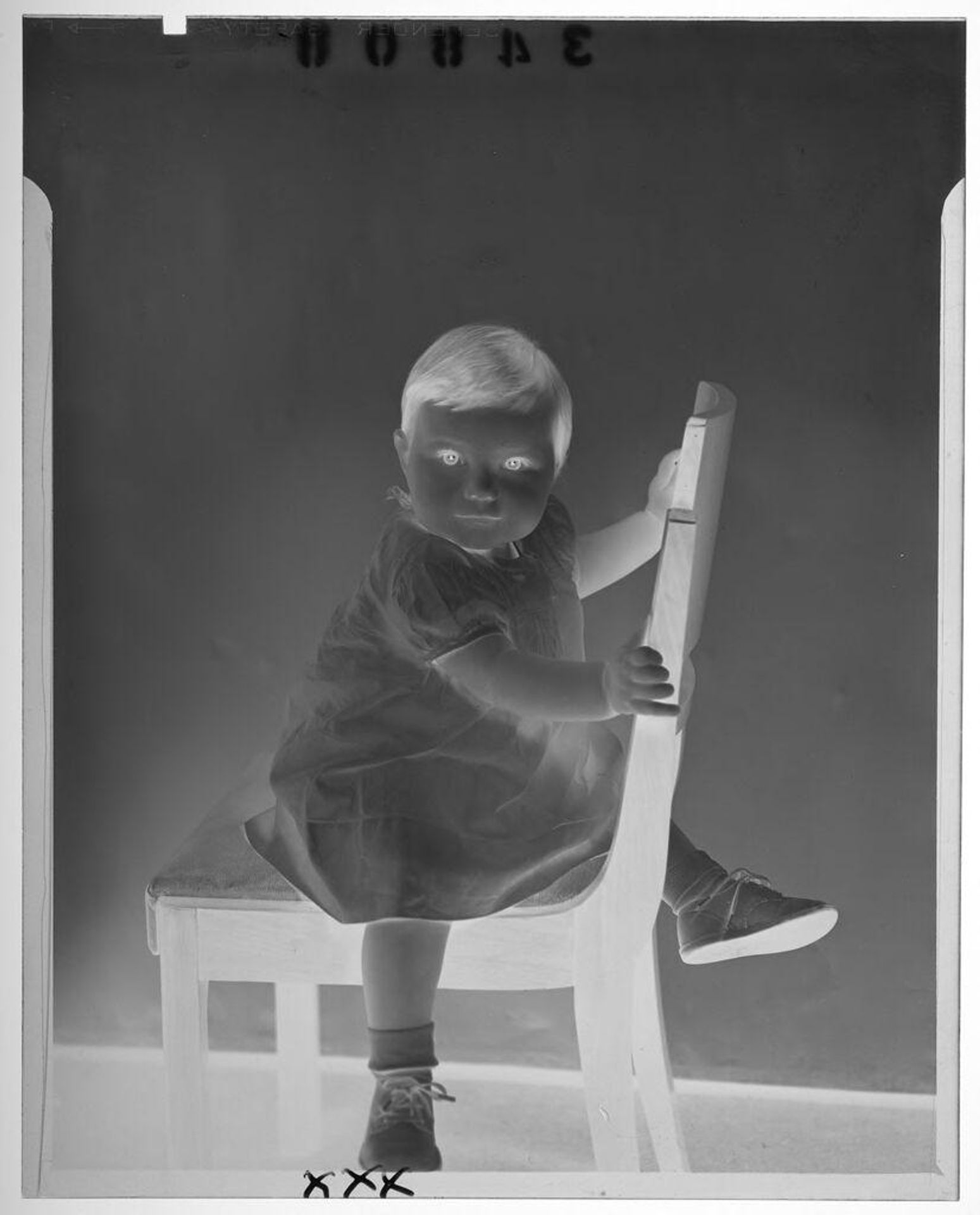 Untitled (studio portrait of baby girl in white dress holding onto chair) by Martin Schweig