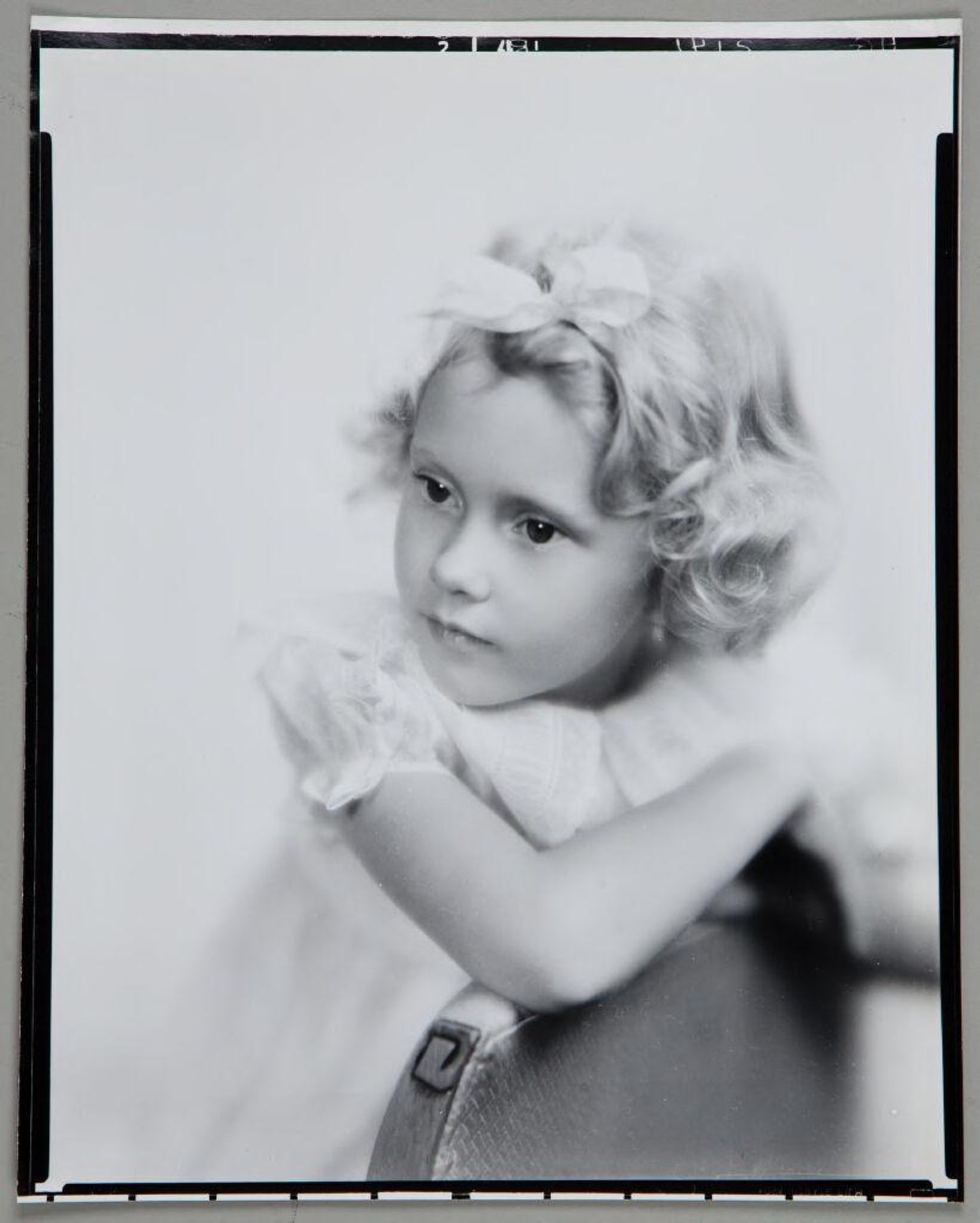 Untitled (portrait of blond girl with bow in hair, arm over back of chair, looking left) by Paul Gittings