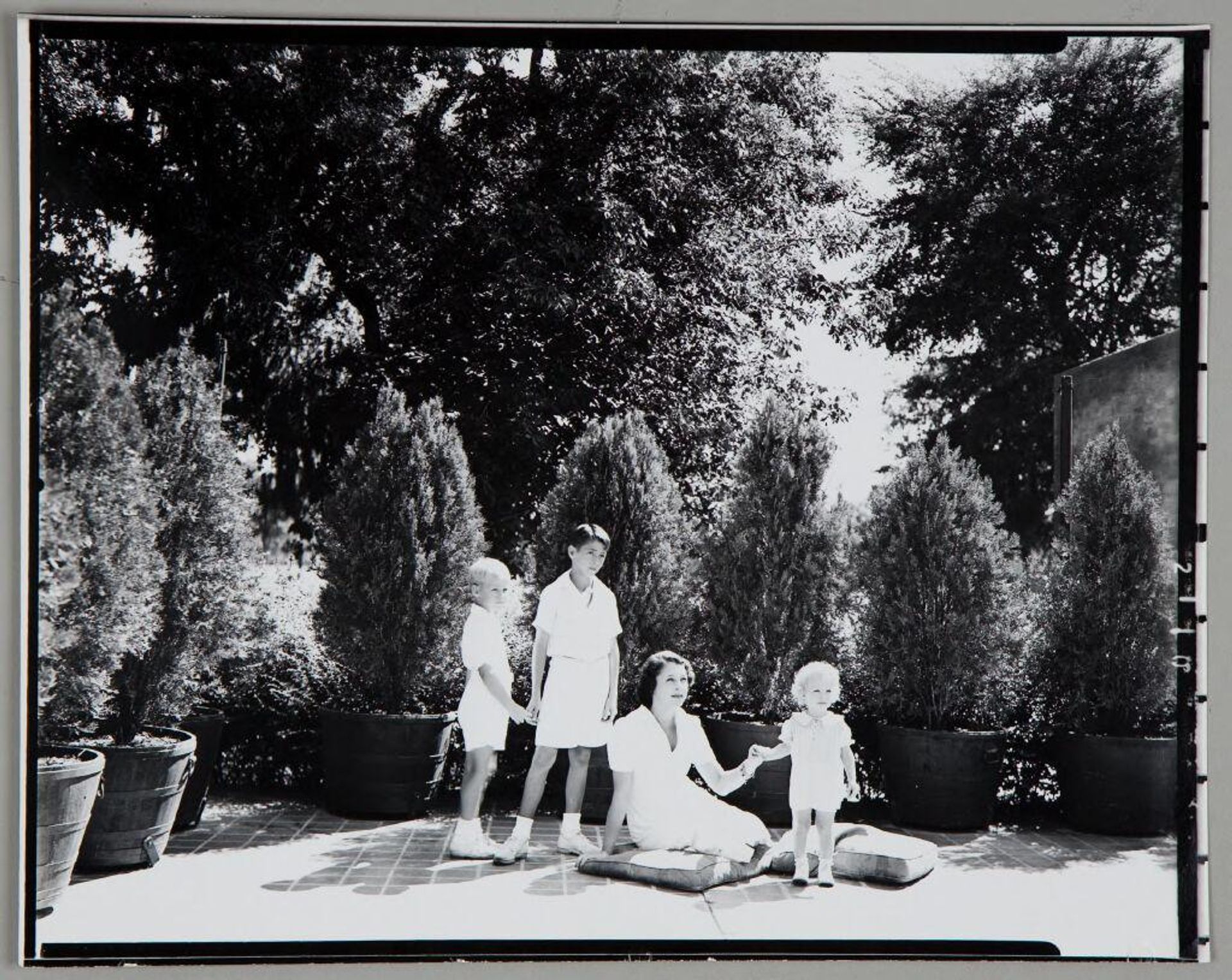 Untitled (woman sitting on patio with two boys and little girl, all dressed in white) by Paul Gittings