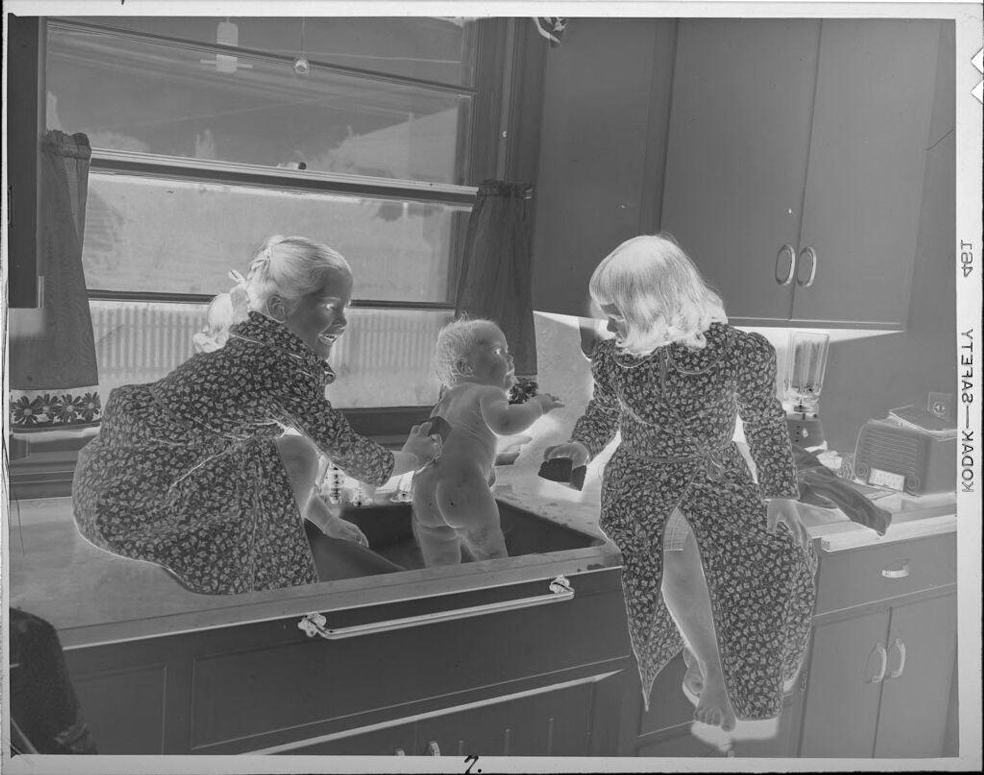 Untitled (girls giving baby a bath in sink) by Lucian and Mary Brown
