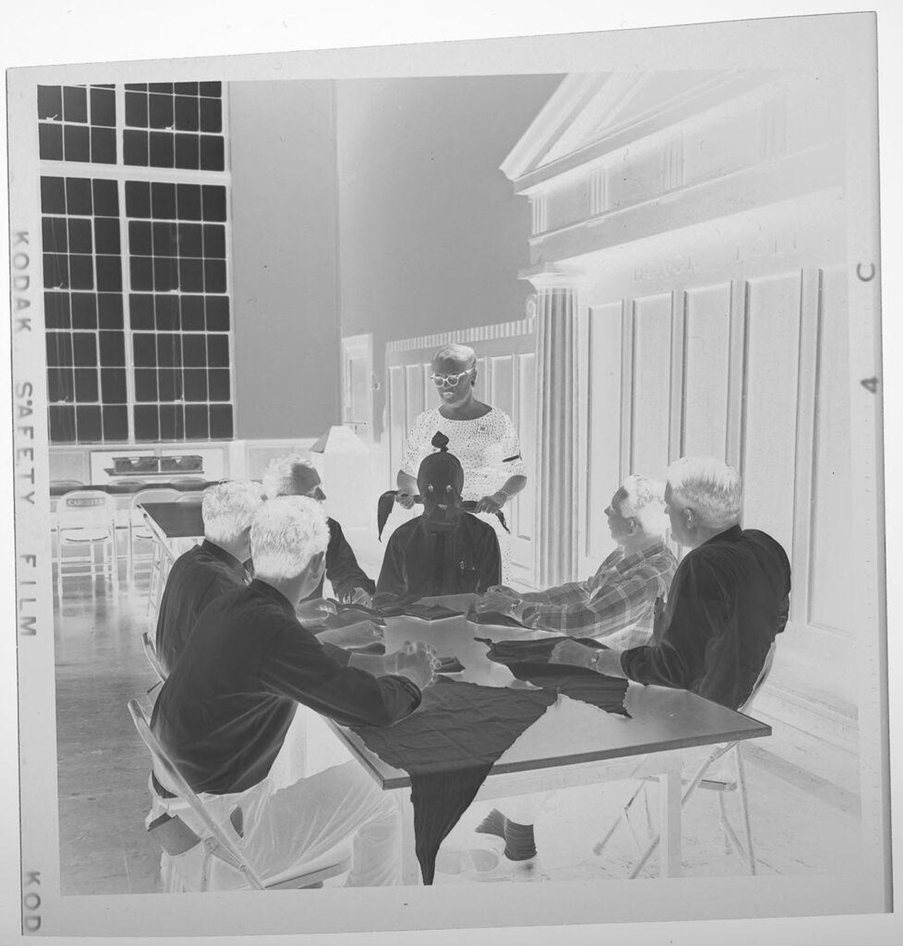 Untitled (people gathered around table learning to tie scarves) by Jack Gould