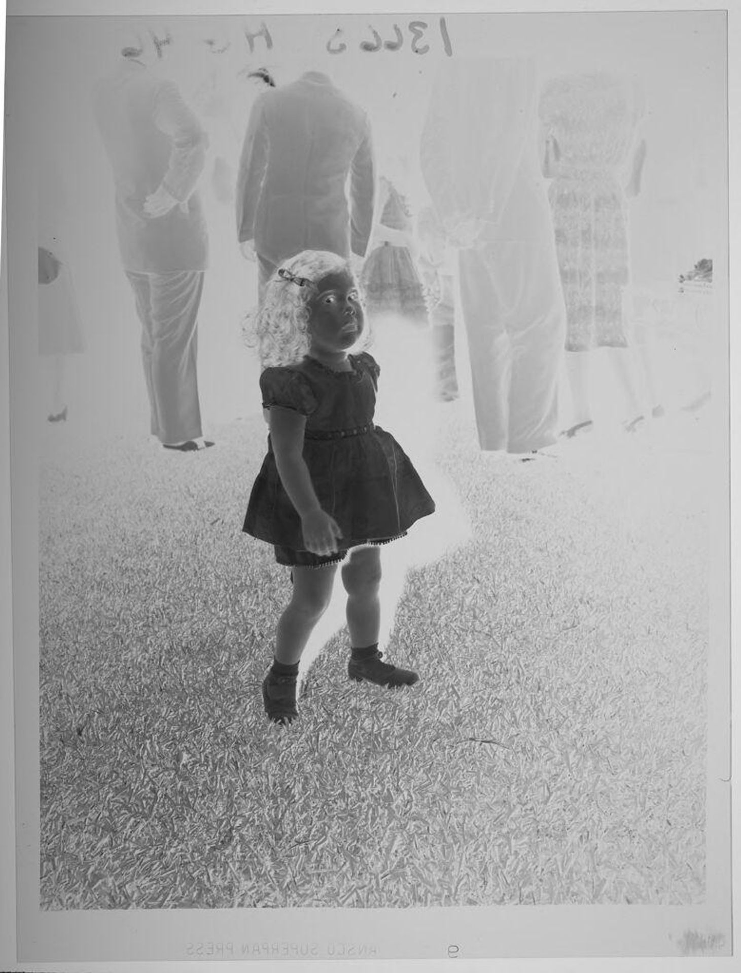 Untitled (little girl standing on grass, group of adults in background) by Paul Gittings