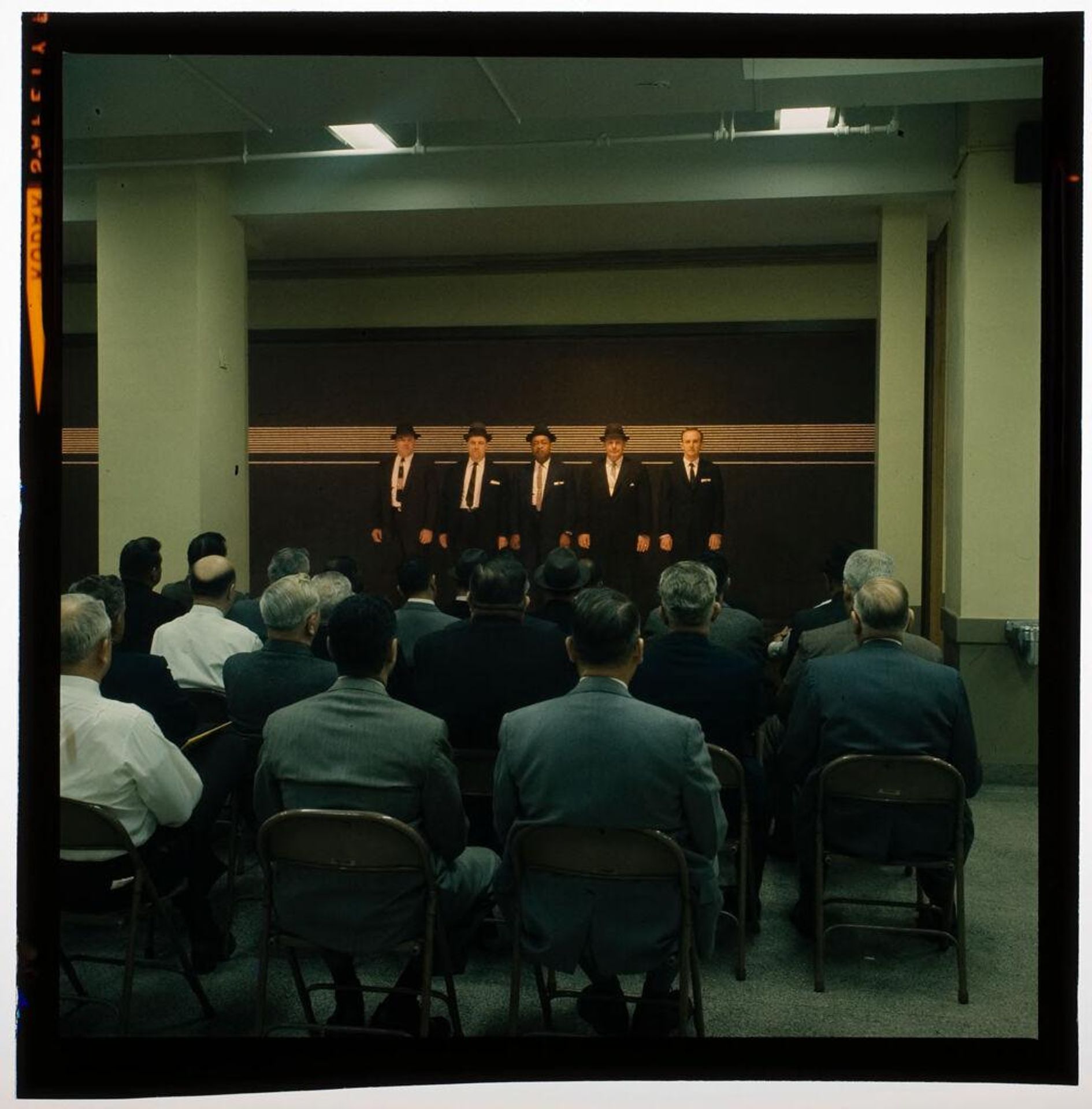 Untitled (men in suits standing in police line-up, audience watching) by Jack Gould