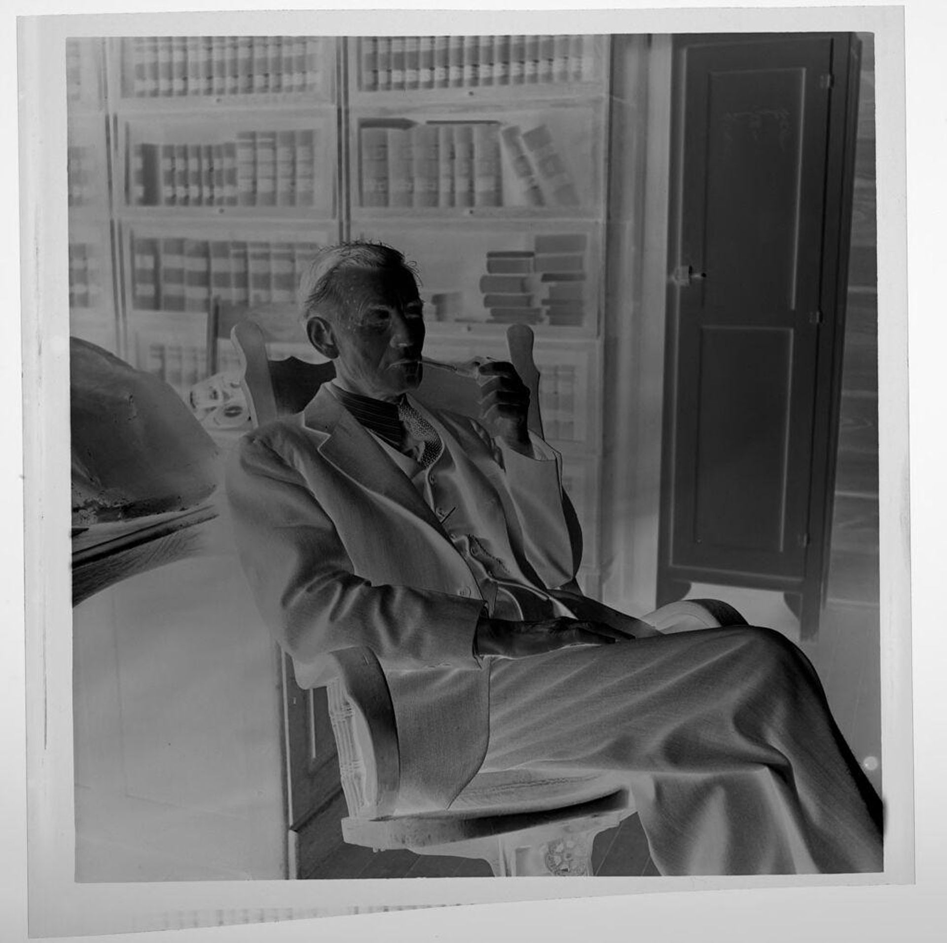 Untitled (elderly man in chair with pipe and bookcase behind) by Jack Gould