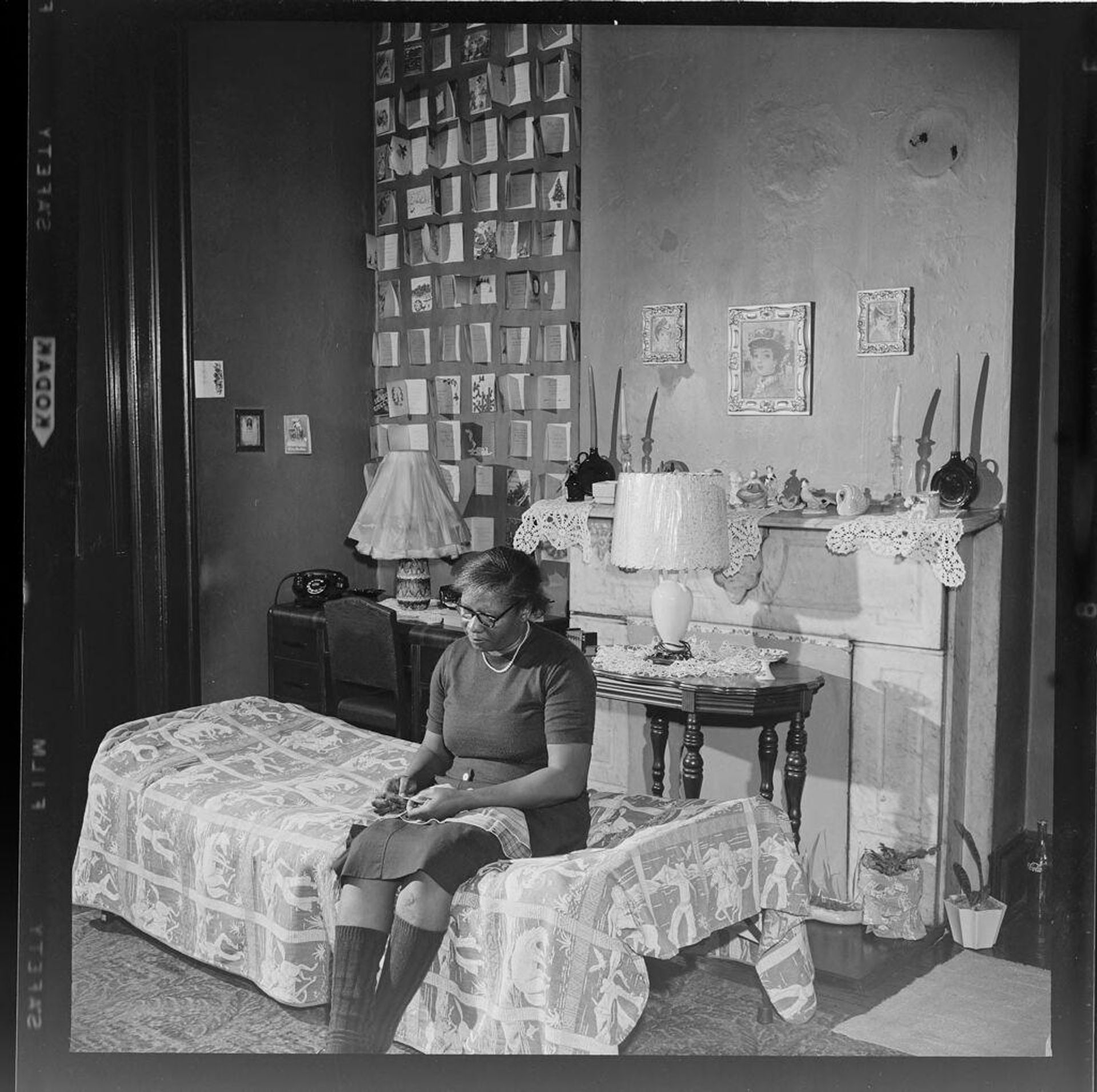 Untitled (woman sitting on bed inside small house) by Jack Gould