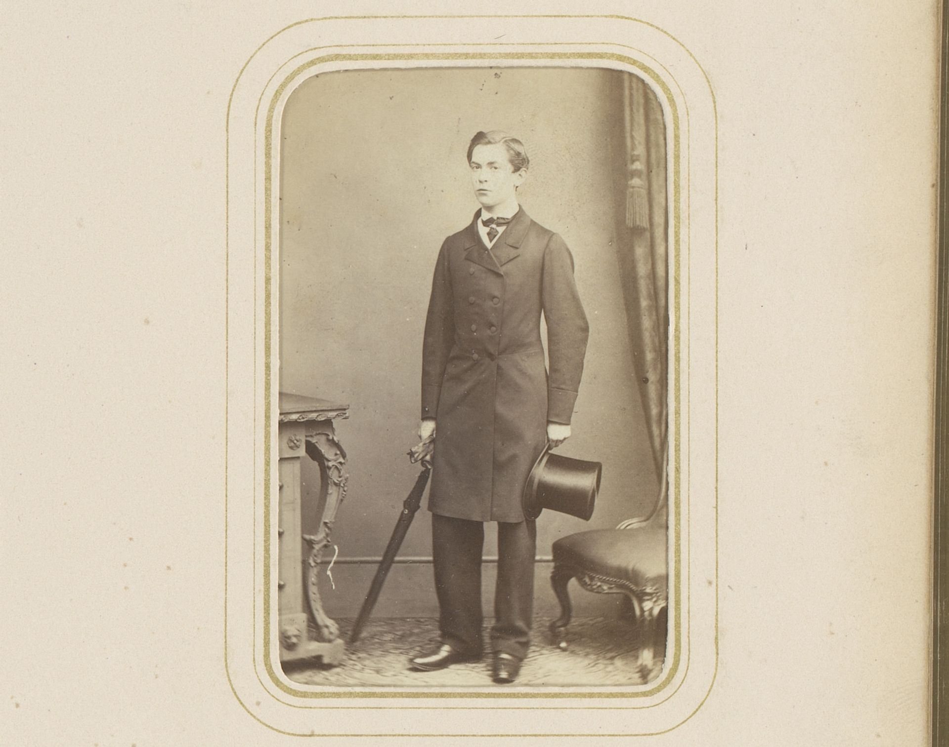 Portret van een staande jonge man met in de ene hand een hoge hoed en in de andere hand een paraplu en handschoenen by Gush & Ferguson