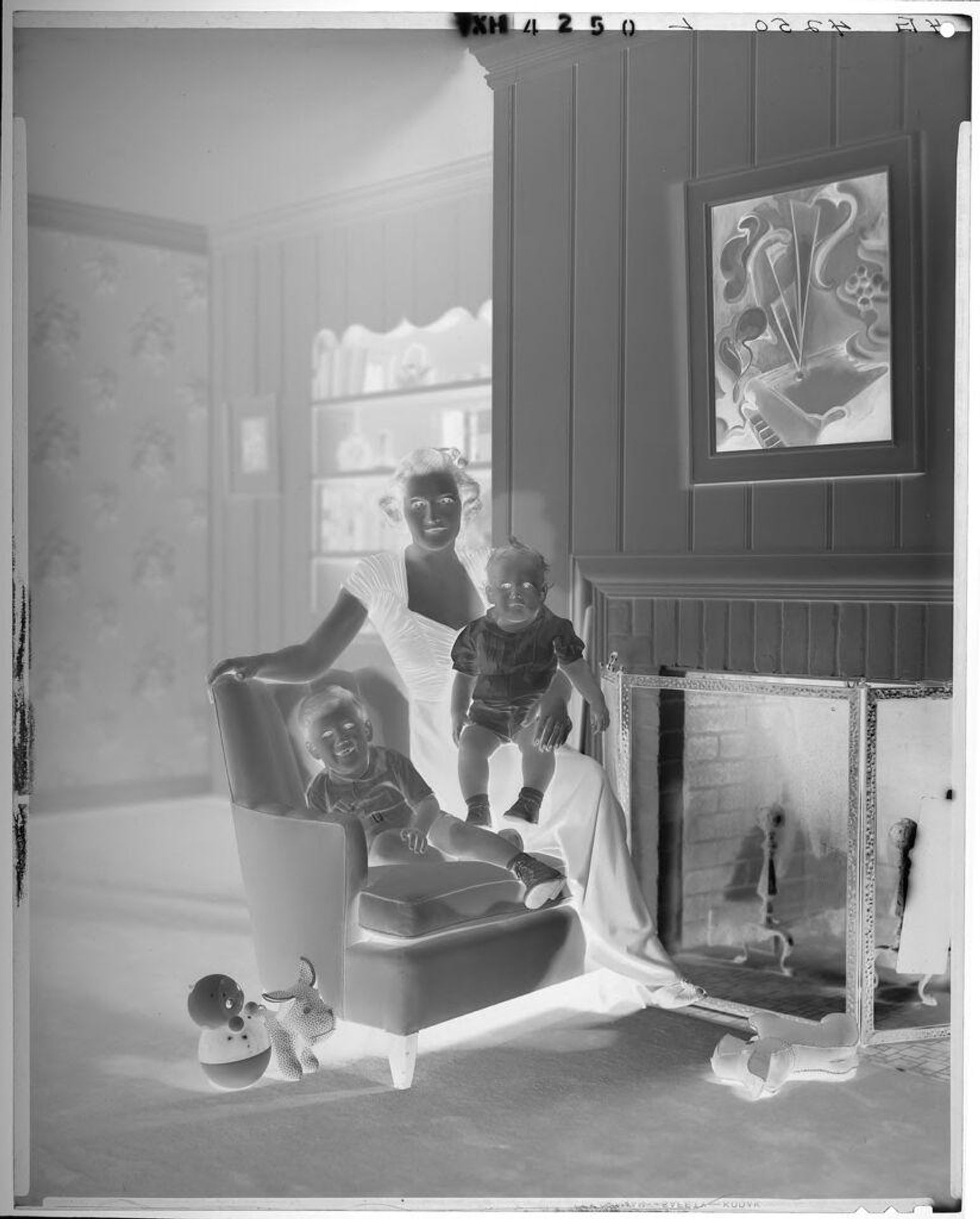 Untitled (woman in long formal dress with children around chair in living room, toys on floor) by Paul Gittings