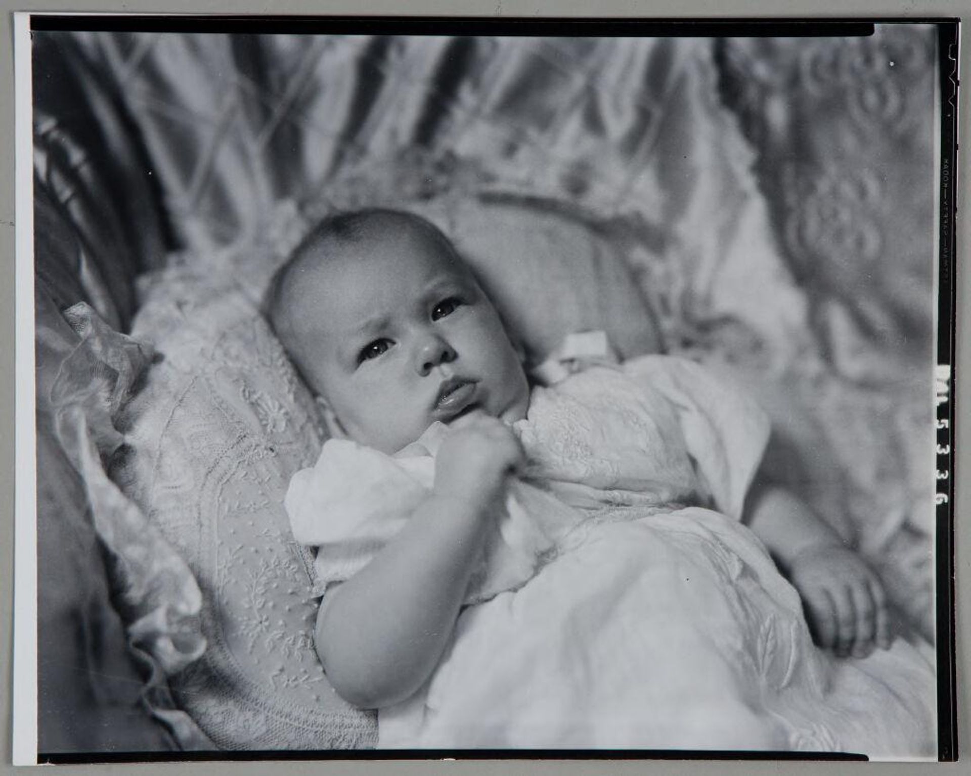 Untitled (baby lying against fancy pillow, fist to chin) by Paul Gittings