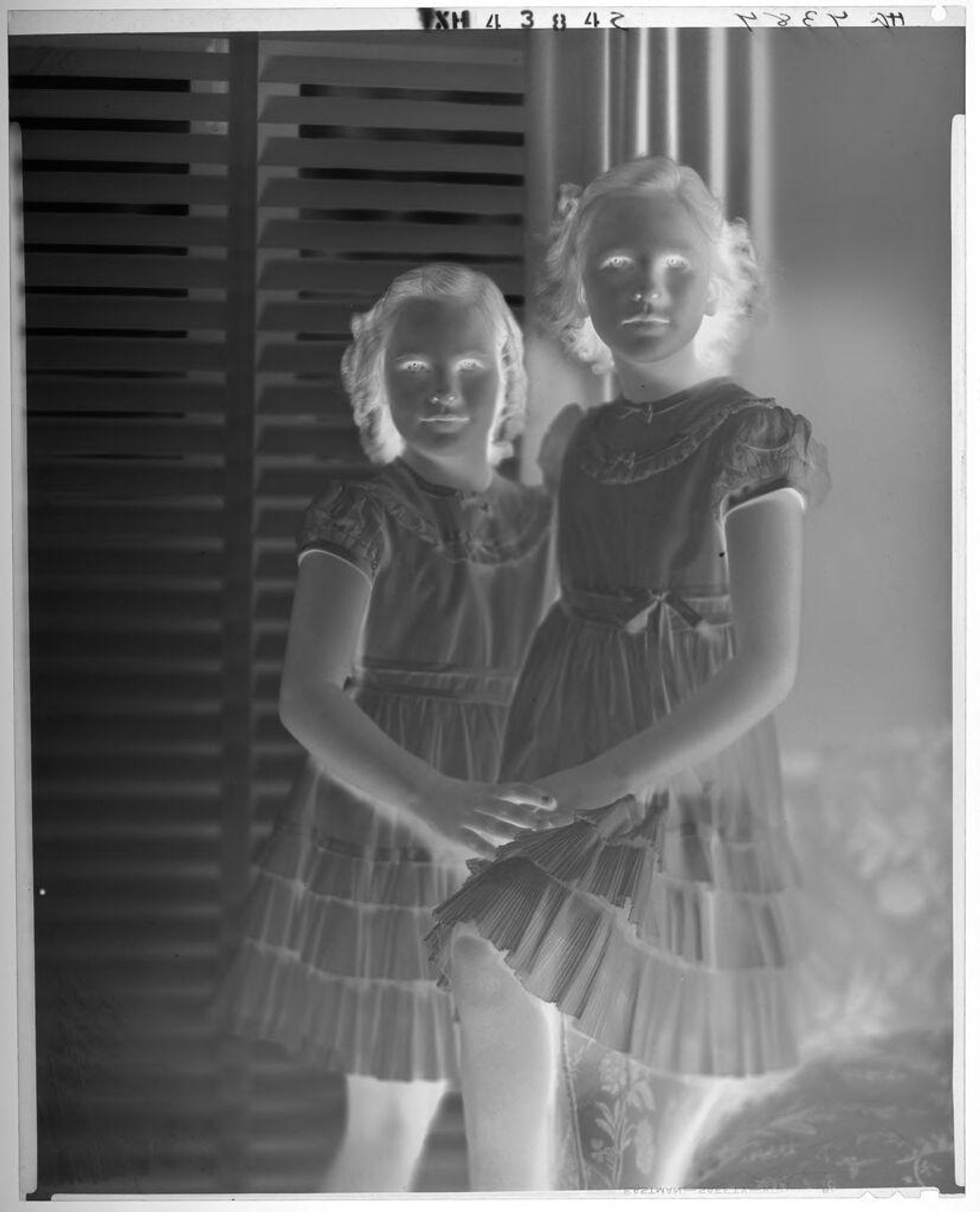 Untitled (two girls in matching dresses standing in front of window with slatted shades) by Paul Gittings