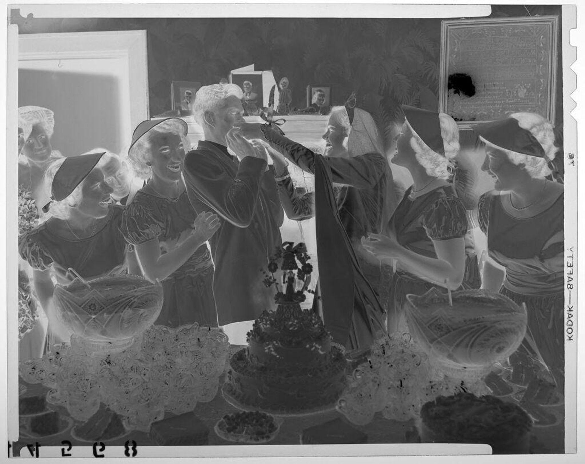 Untitled (bride feeding cake to groom in front of cake table in living room surrounded by bridesmaids) by Martin Schweig