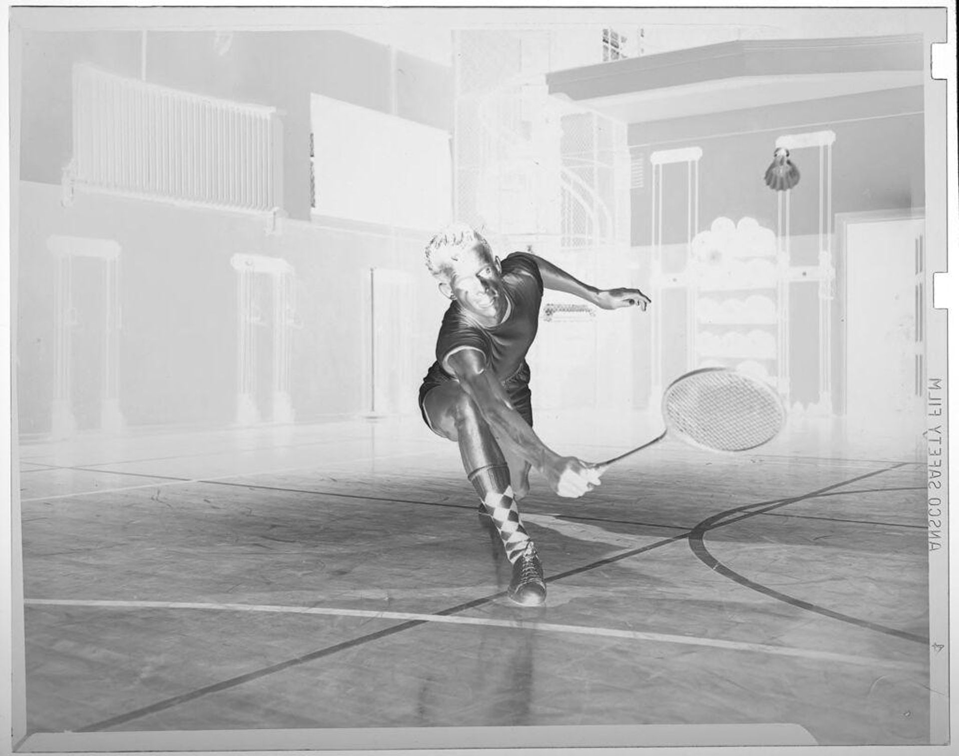 Untitled (man playing indoor badminton, lunging down to hit shuttlecock) by Jack Gould